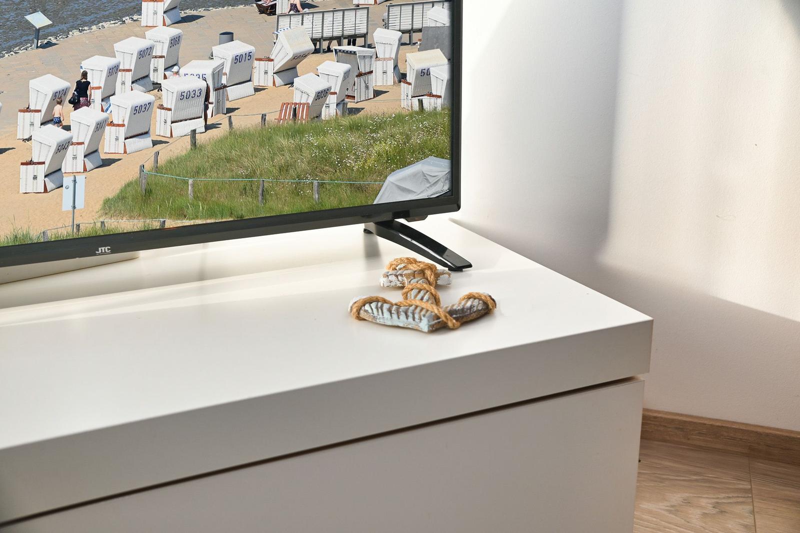 TV auf weißem Möbelstück mit Strandbild und Sandalen darauf.