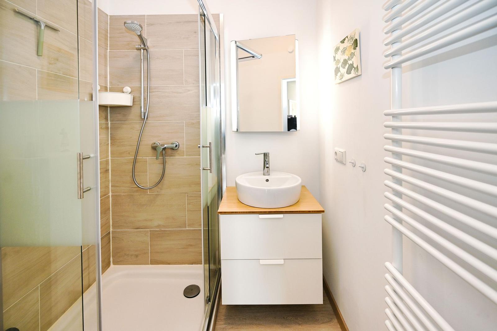 Badezimmer mit Dusche, Waschbecken und Heizkörper