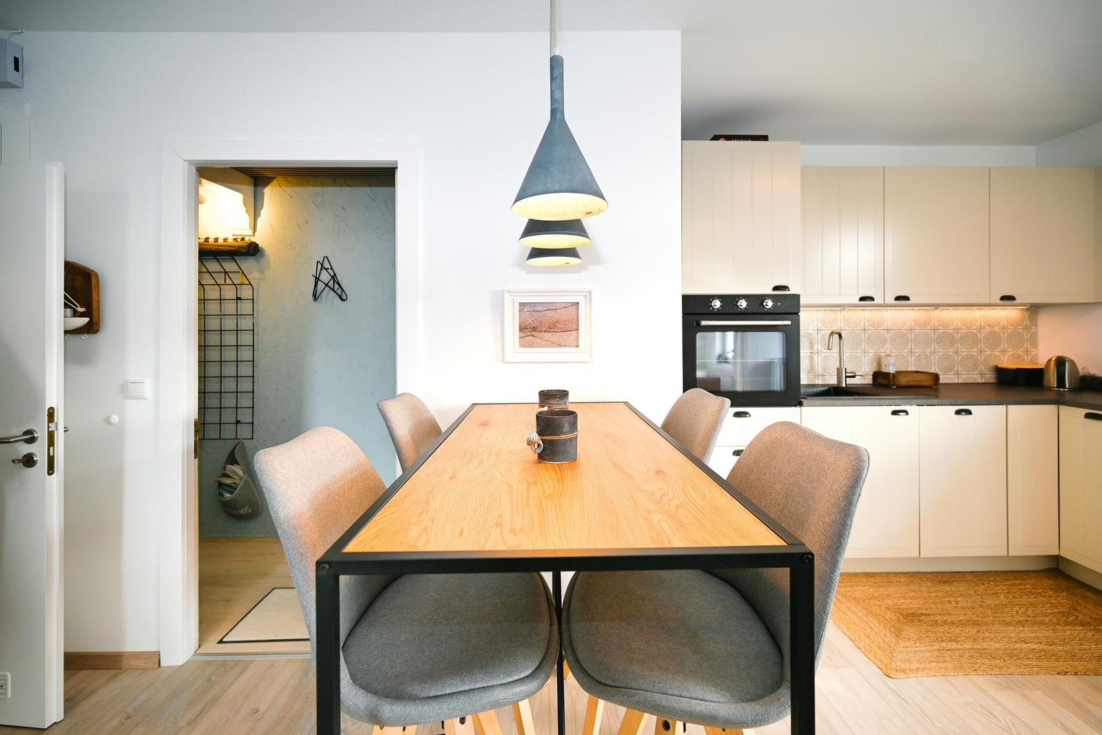 Essbereich mit Tisch und Stühlen, Küche mit weißen Schränken und Dunstabzug.