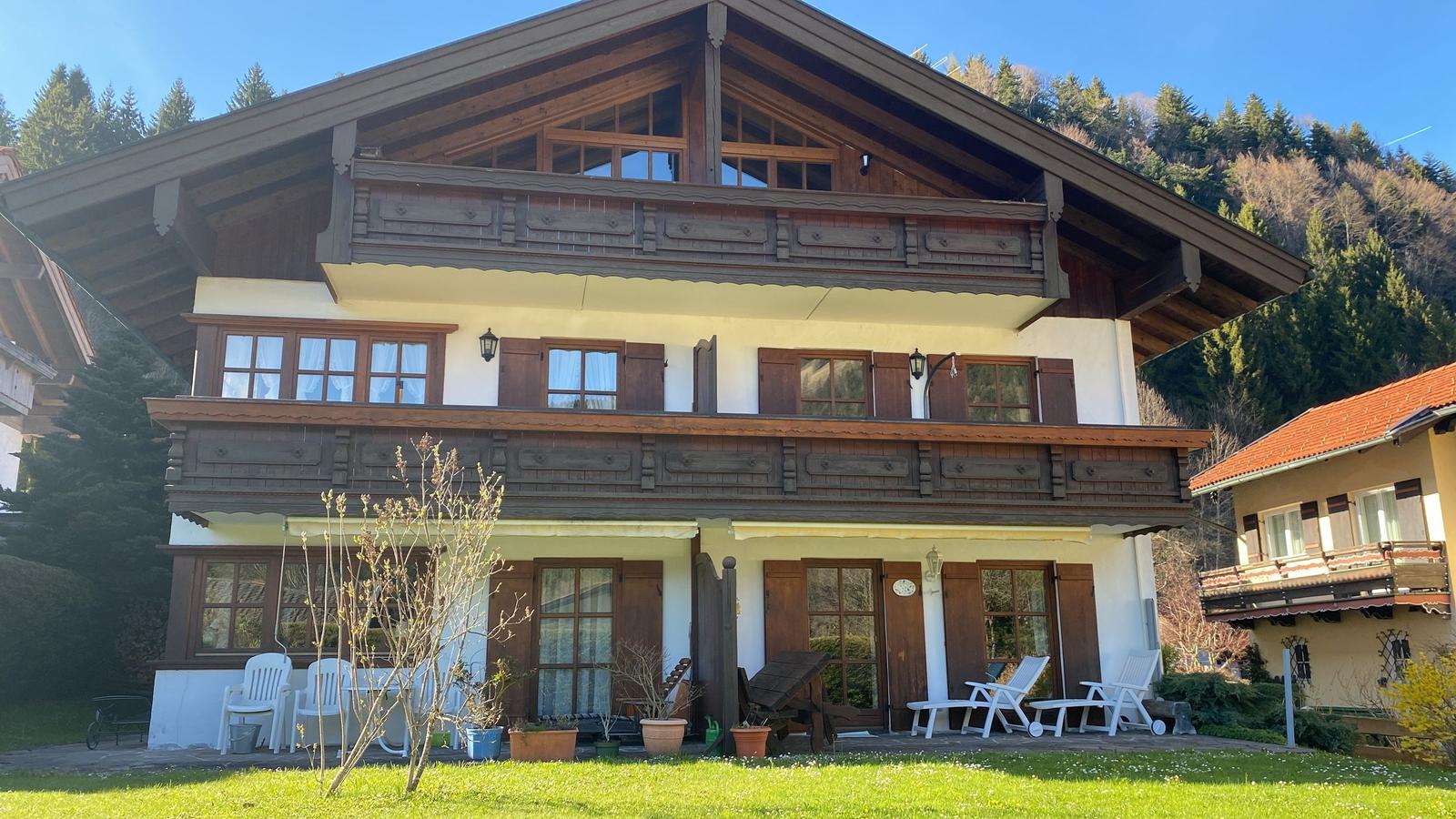 A two-story house with balconies and a garden. White chairs are outside.