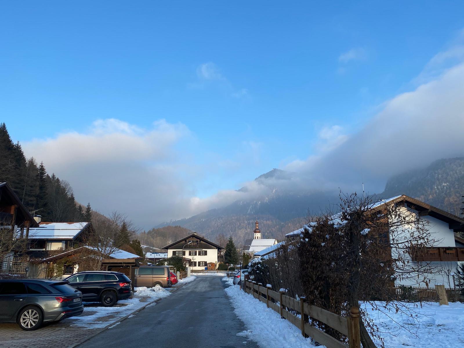Snow-covered street with houses and mountains in the background.