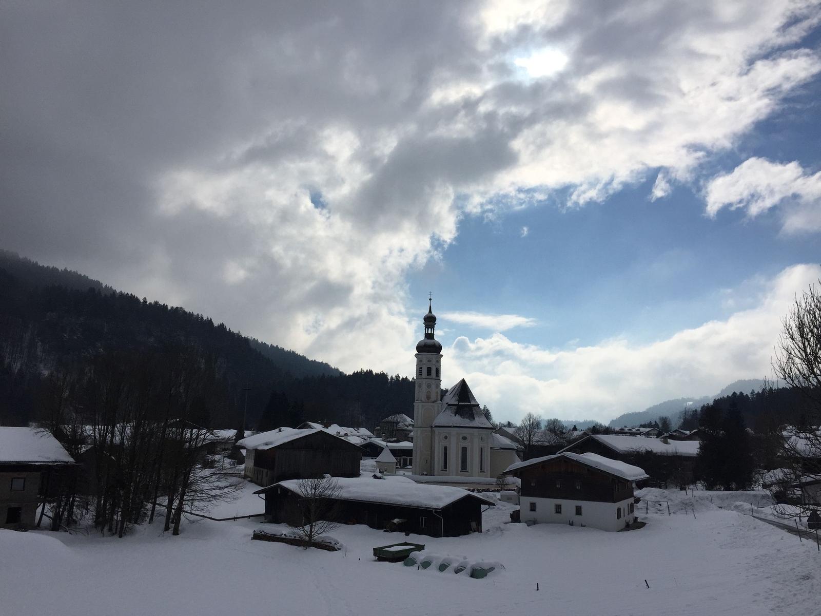Snow-covered houses and a church in the village under a cloudy sky.
