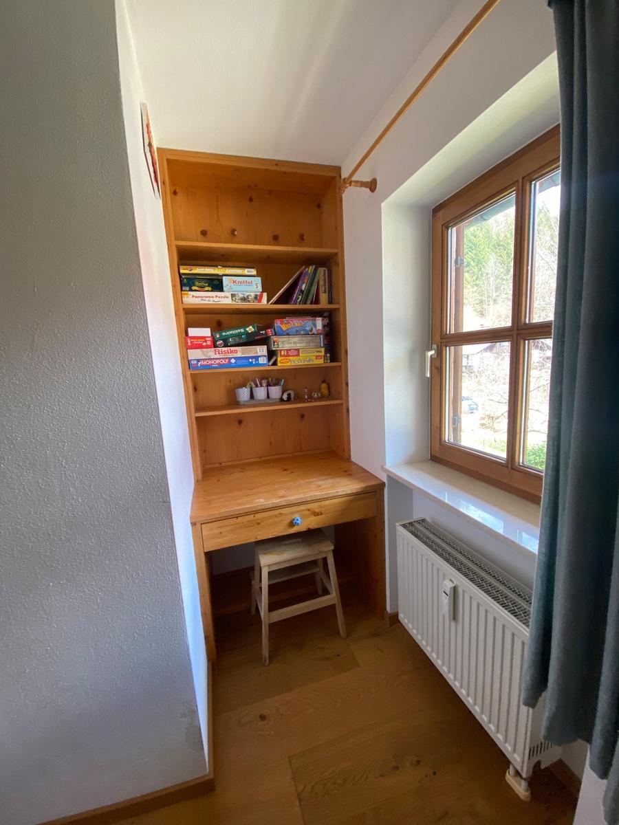 Wooden desk with shelf and stool next to window with view outside.