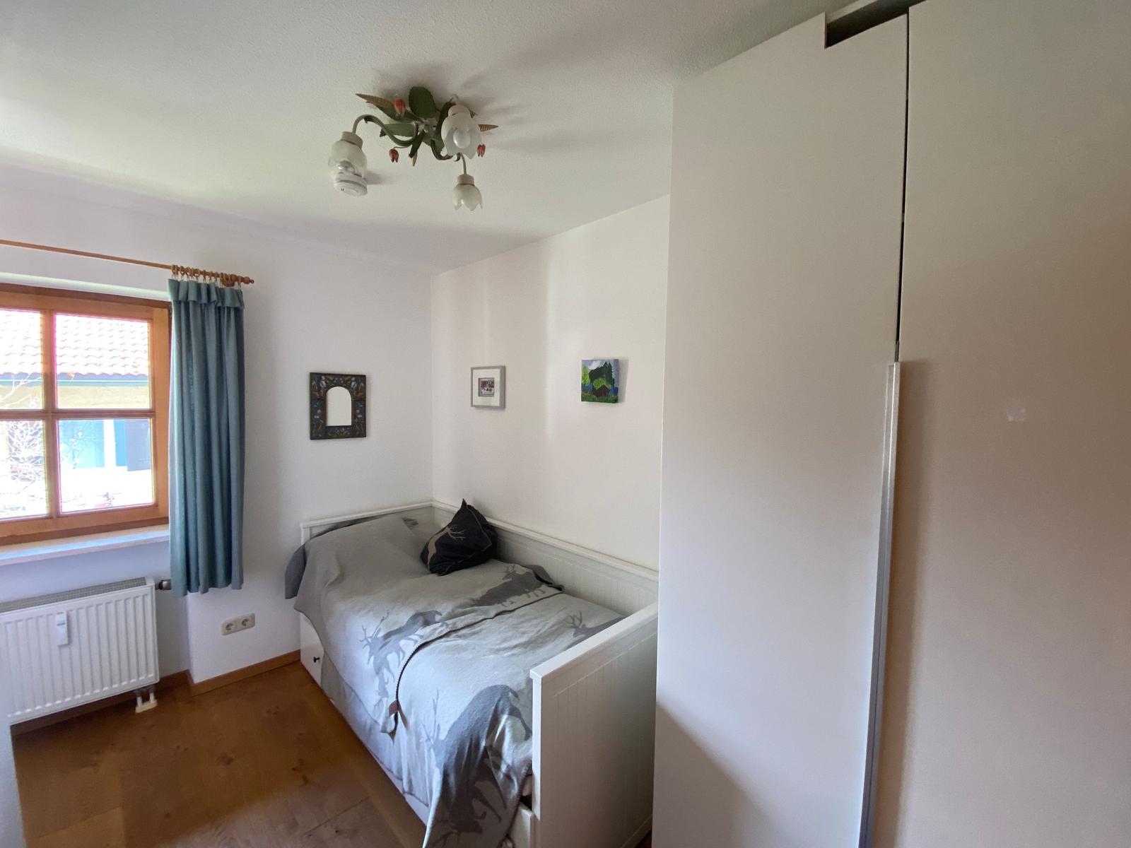 A bedroom with bed, wardrobe, and window with curtain.