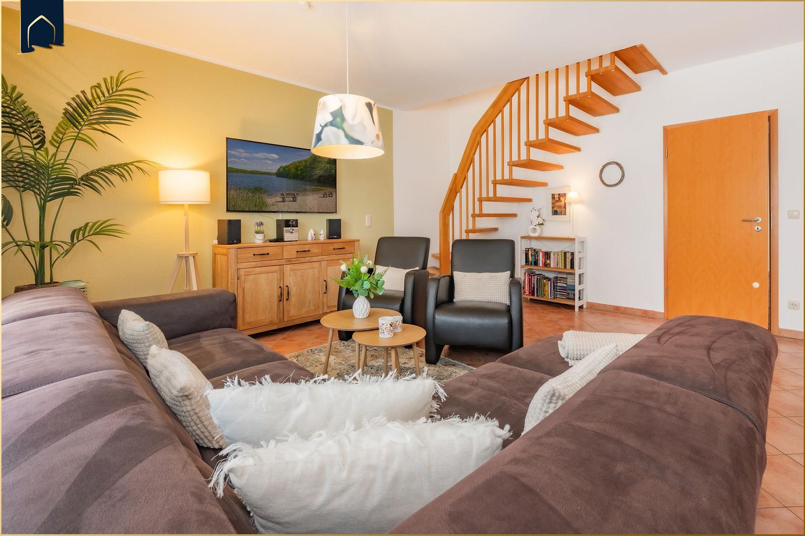 Wohnzimmer mit Sofa, Fernseher und Holztreppe.