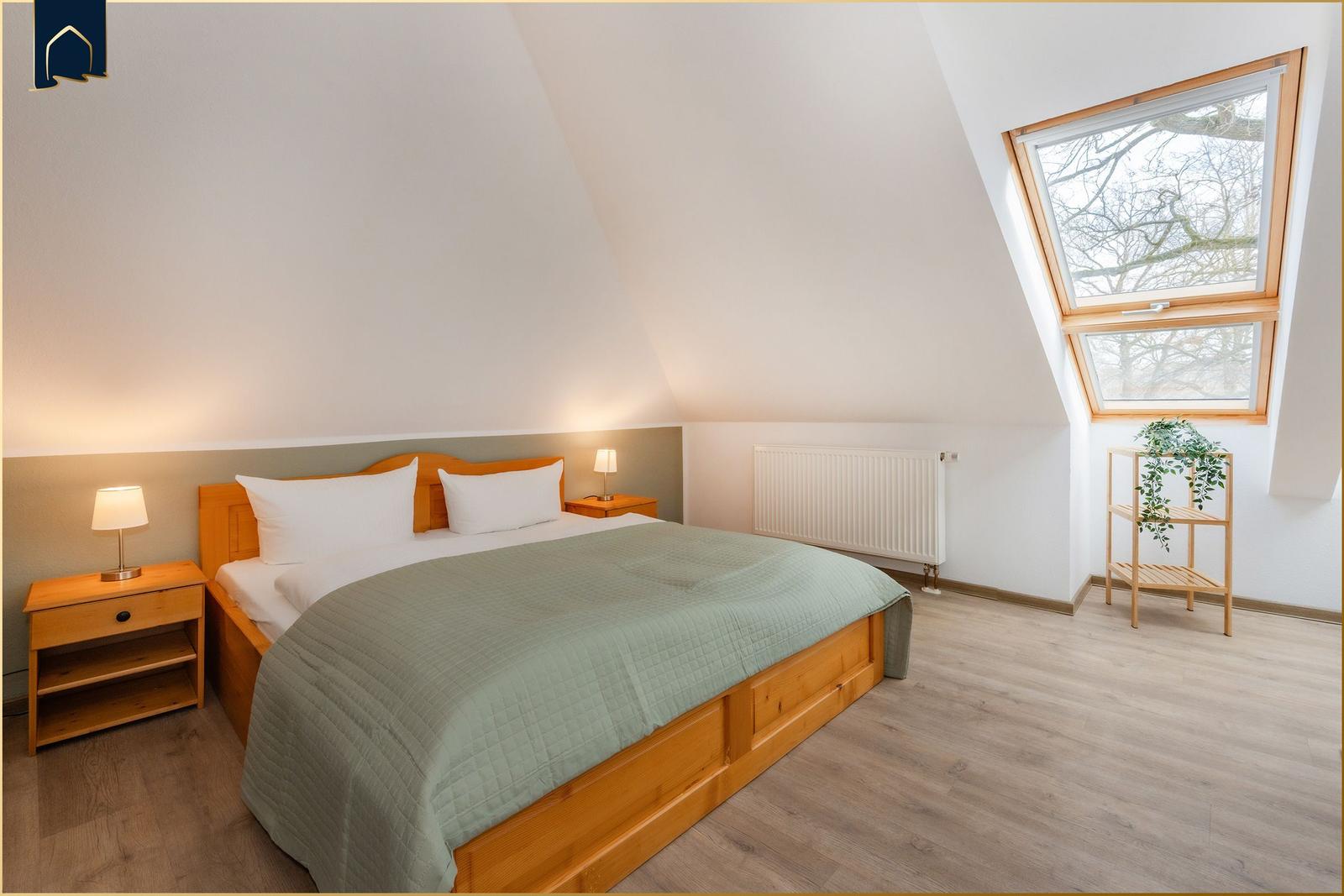 Schlafzimmer mit Dachschräge, Bett, Nachttisch und Fenster.