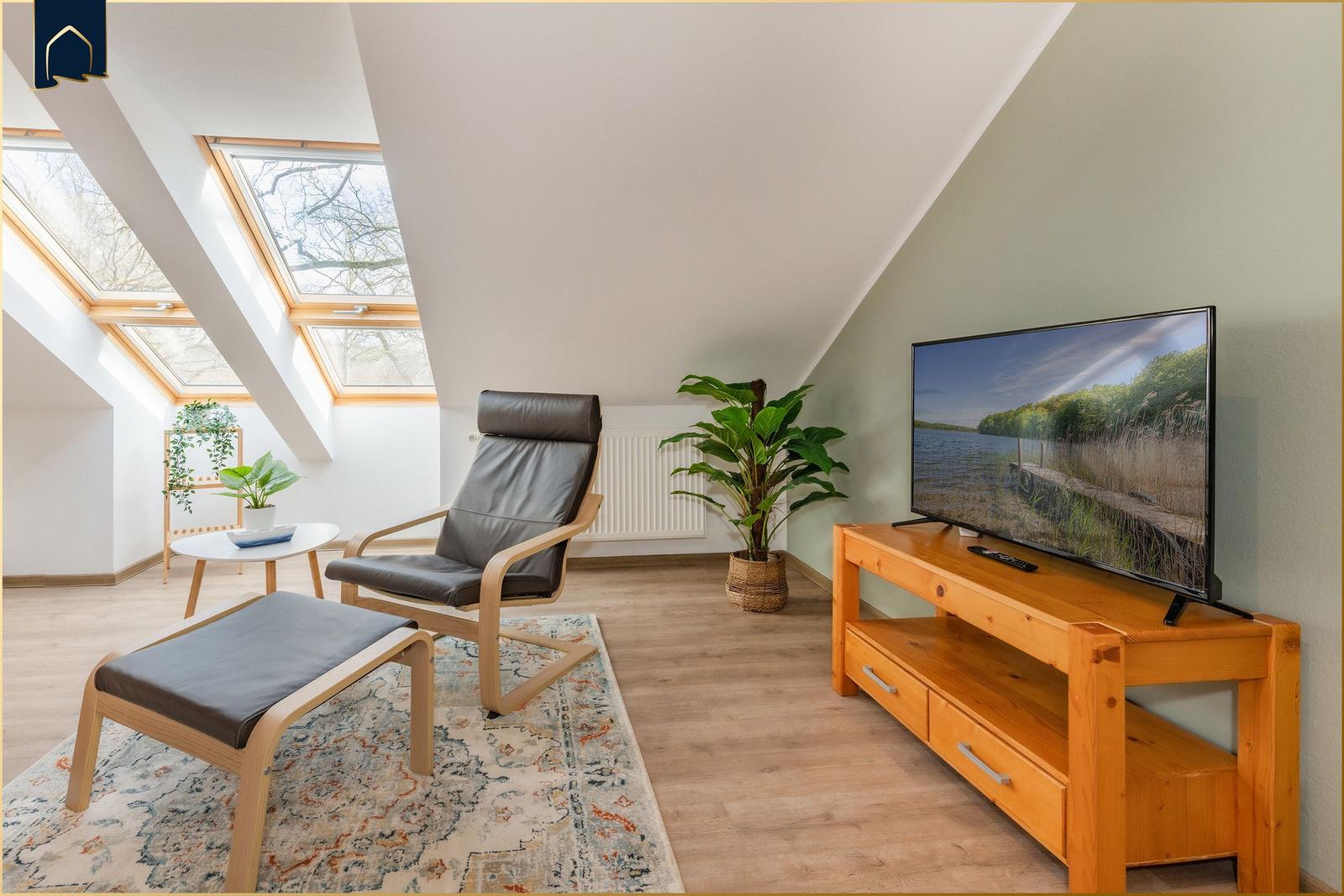 Dachgeschosszimmer mit Sitzgelegenheit, Fernseher und Dachfenstern.
