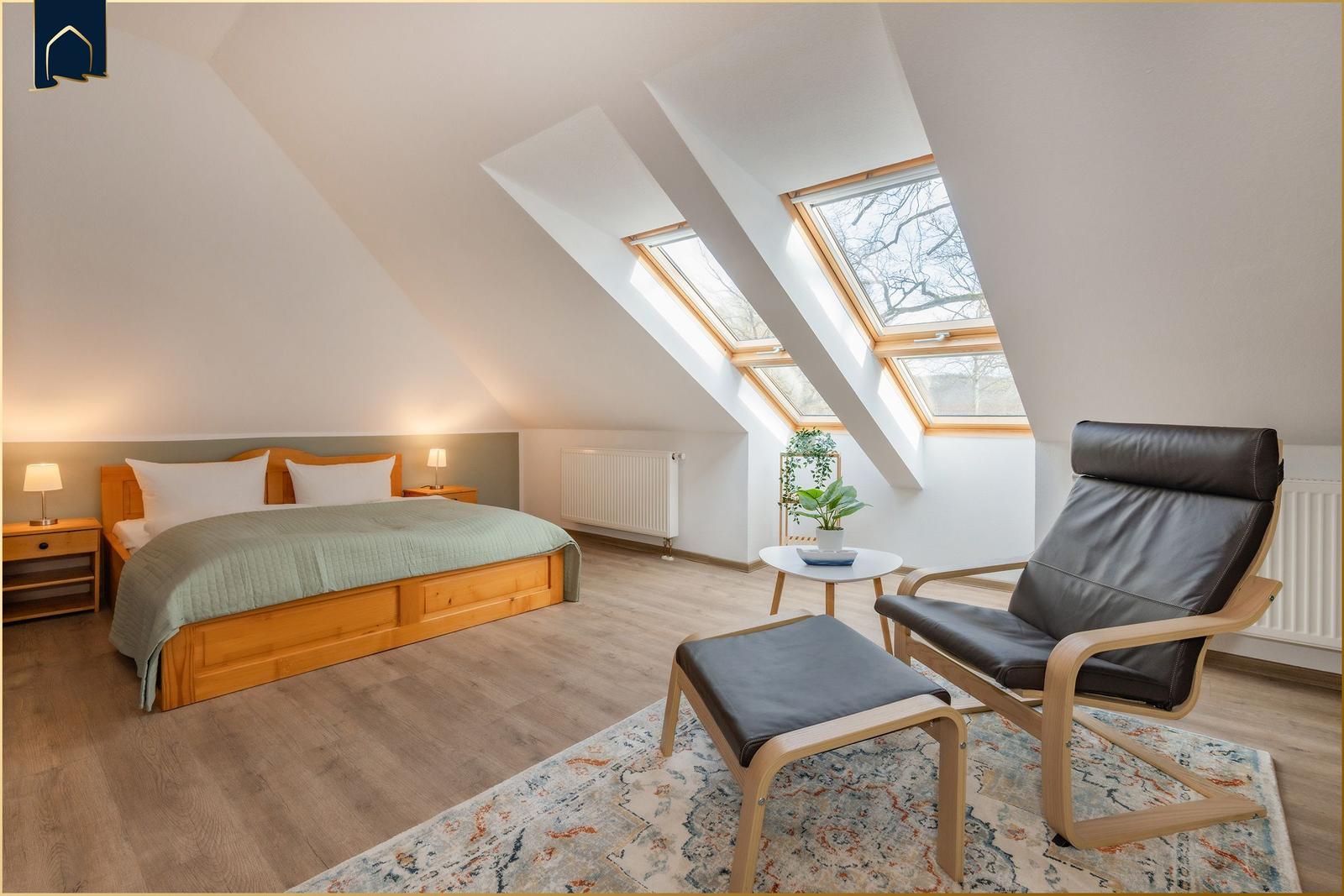 Schlafzimmer mit Dachschrägen, Dachfenstern, Bett und Sessel.