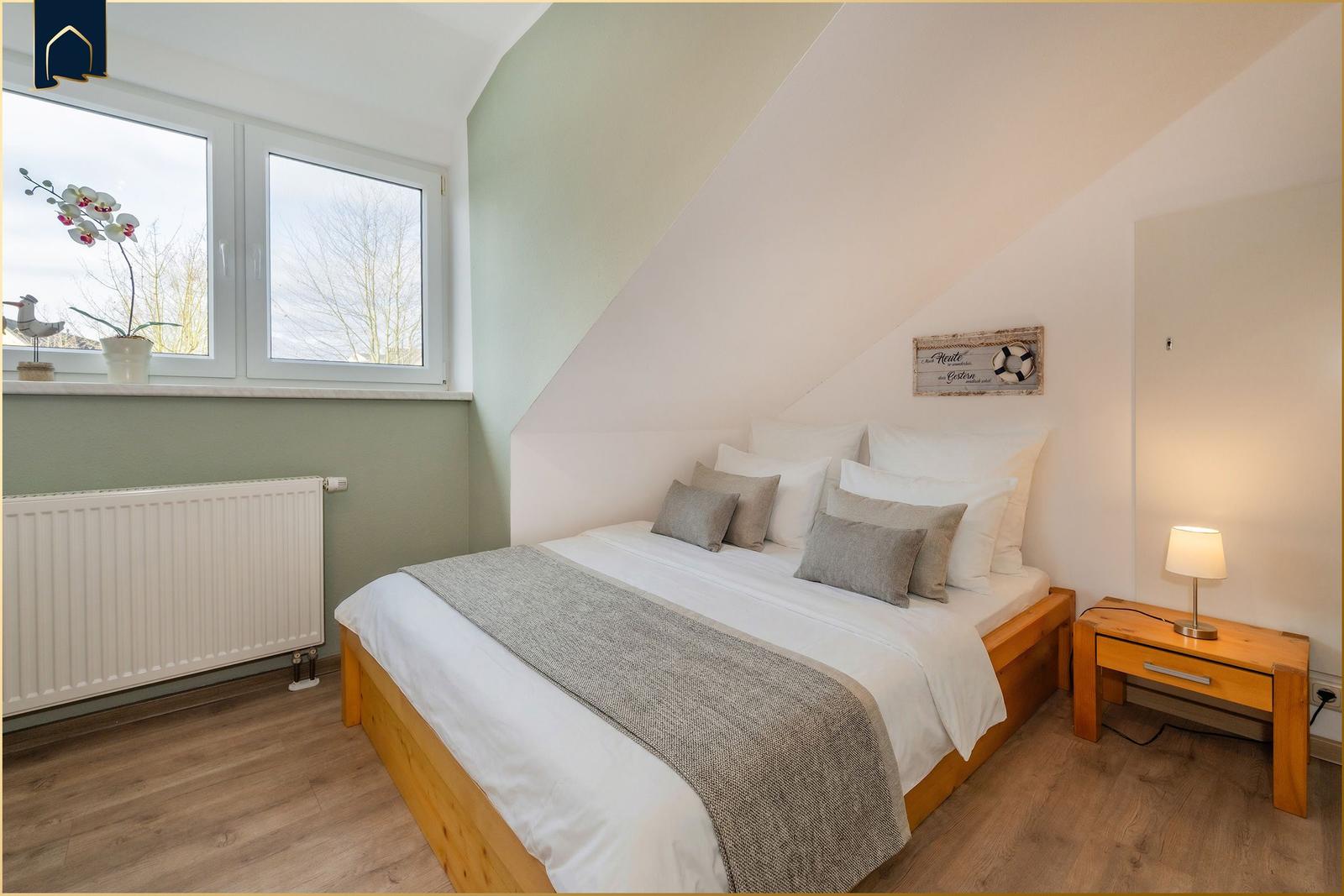 Schlafzimmer mit Dachschrägen, Bett, Nachttisch und Fenster.
