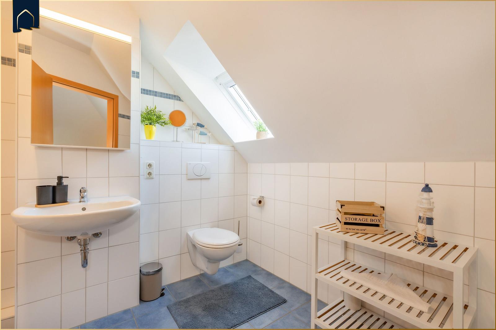 Badezimmer mit Dachschrägen, Waschbecken, Toilette und Holzregal.