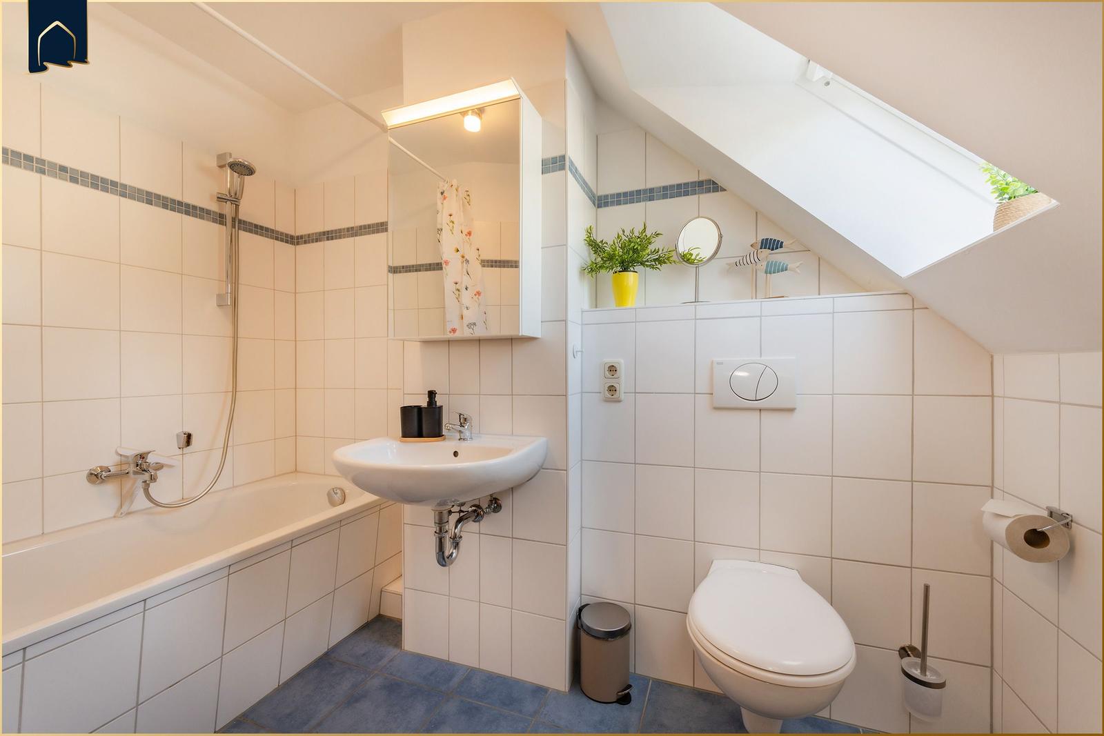 Badezimmer mit Badewanne, Waschbecken und Toilette unter Dachschräge mit Dachfenster.