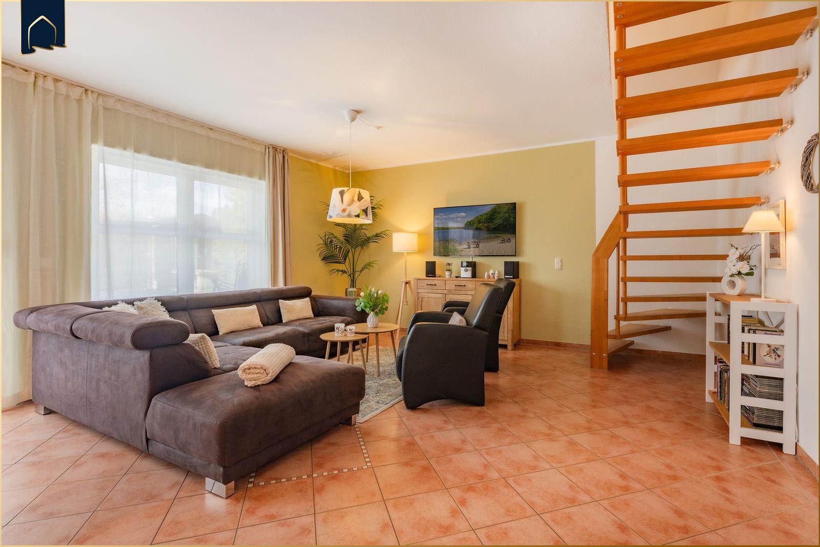Wohnzimmer mit Sofa, Sessel und Holztreppe.