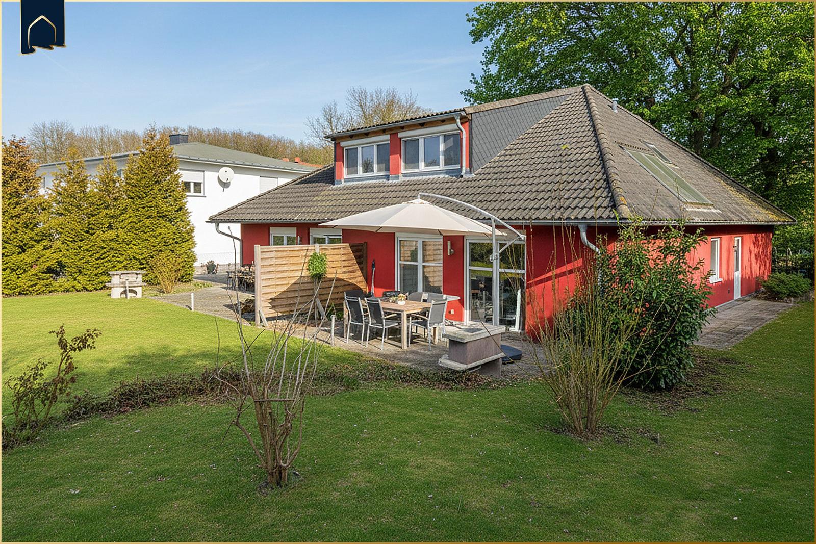 Rotes Haus mit Garten, Terrasse und Sonnenschirm. Holzumzäunung und Grillplatz.