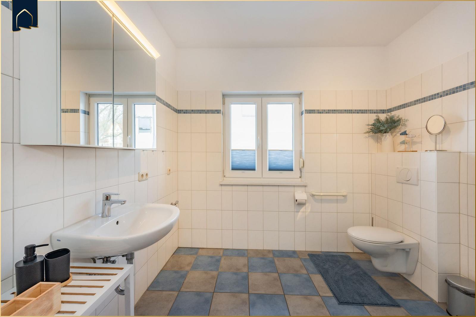 Badezimmer mit Waschbecken, Toilette und Fenster. Fliesenboden und Spiegelschrank.