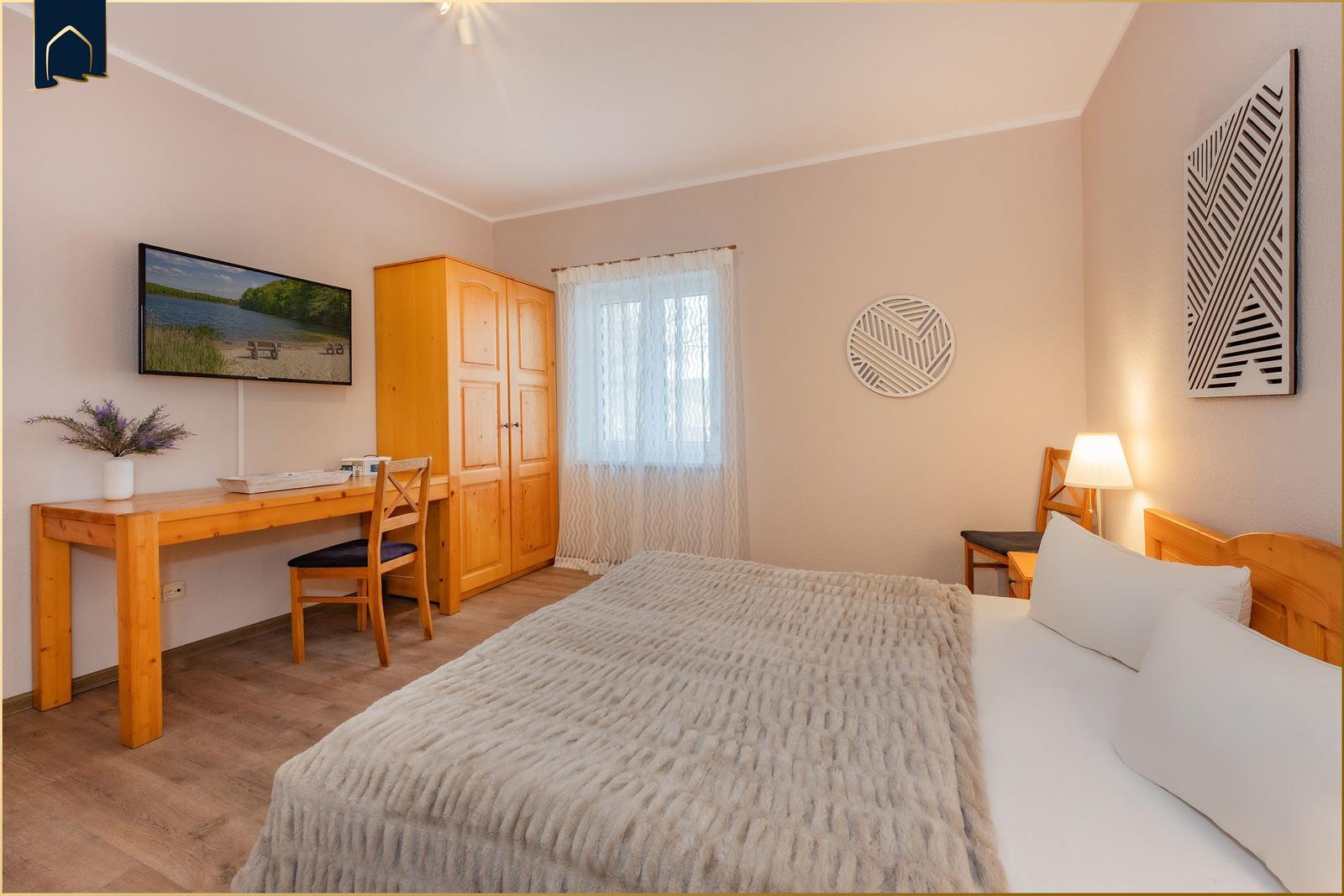 Schlafzimmer mit Bett, Schreibtisch, Kleiderschrank und Fenster.