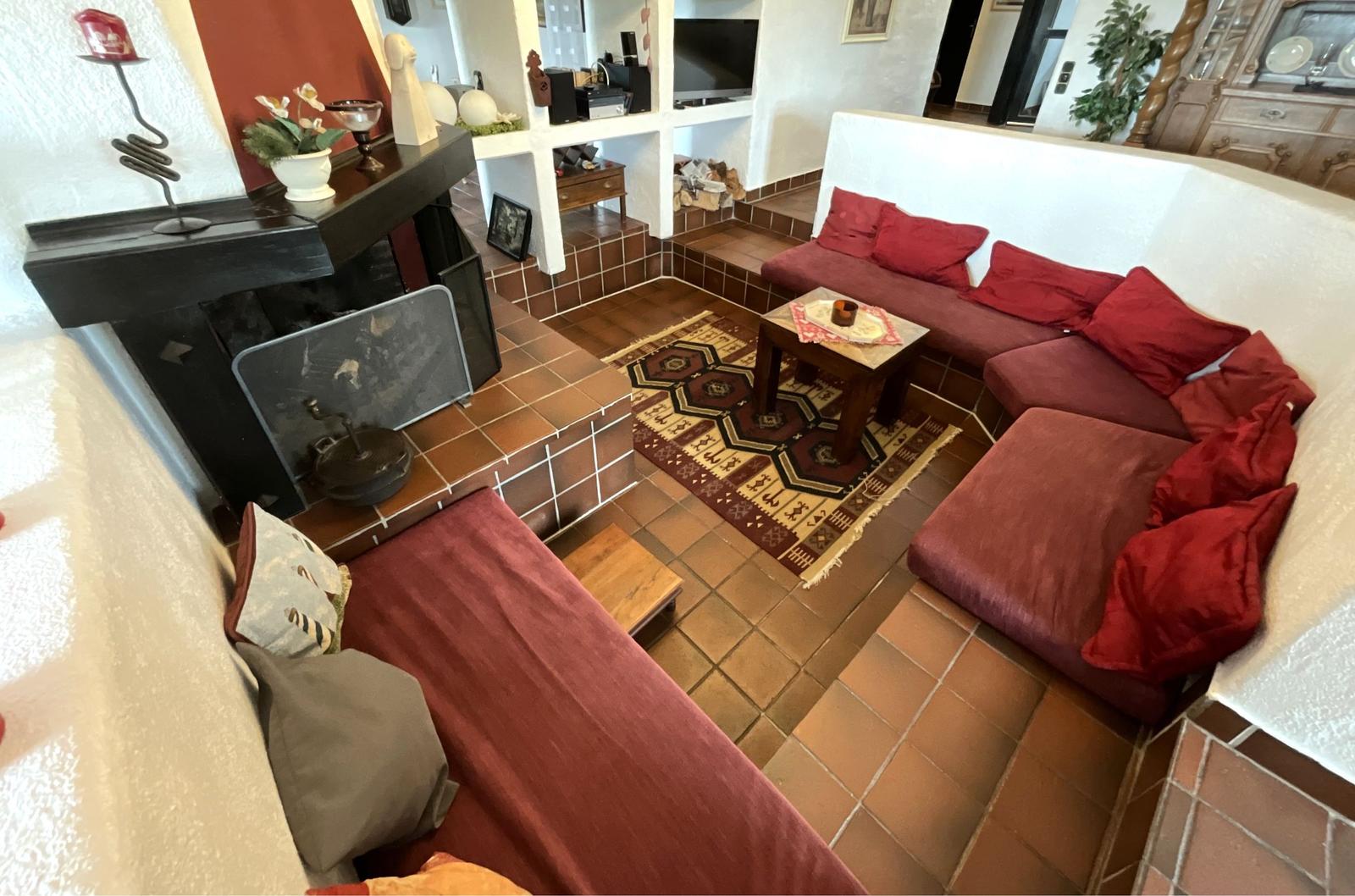 Wohnzimmer mit rotem Sofa, Kamin und Teppich auf Fliesenboden.