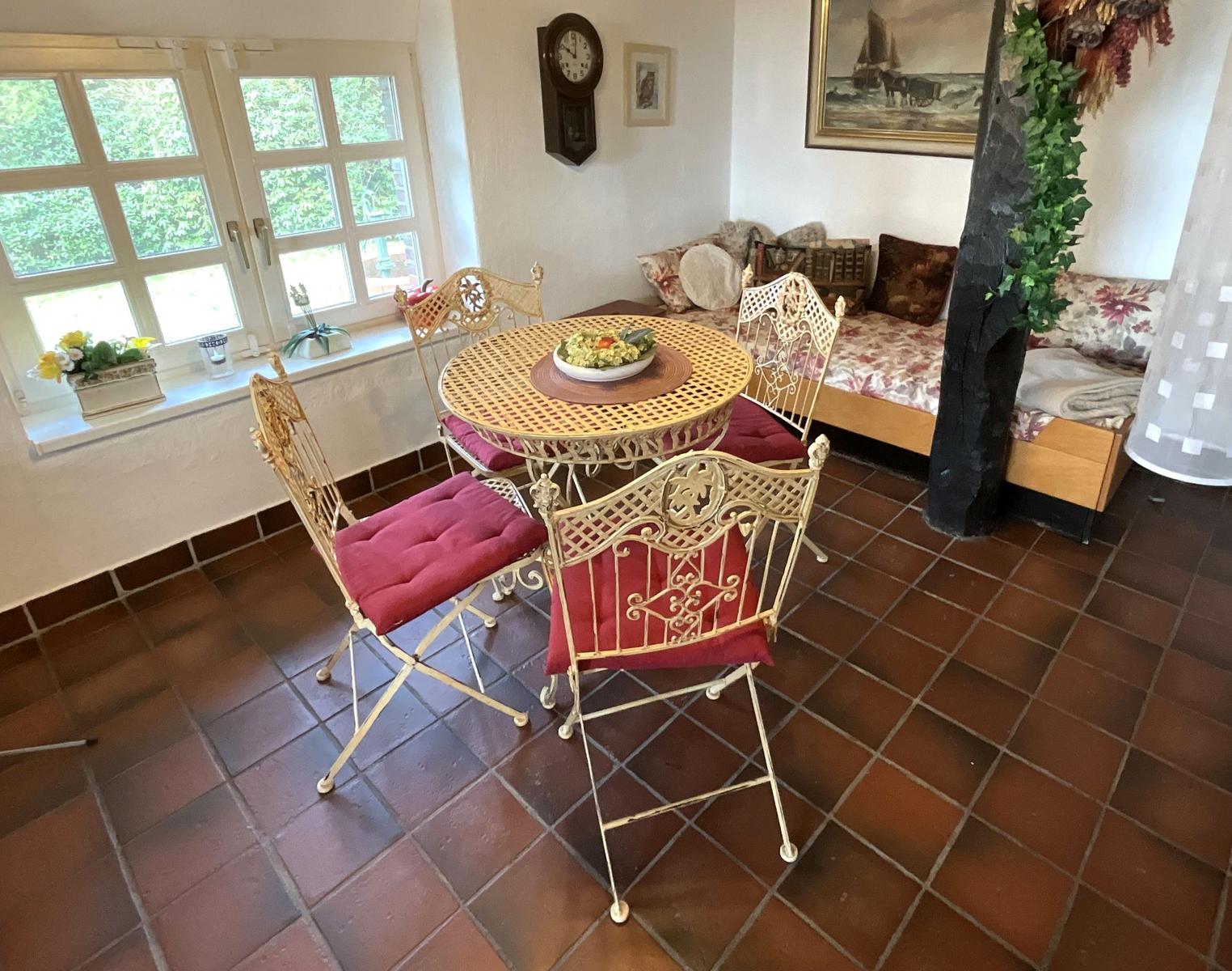 Esszimmer mit Tisch, Stühlen und Fenster. Im Hintergrund Sofa und Wanduhr.