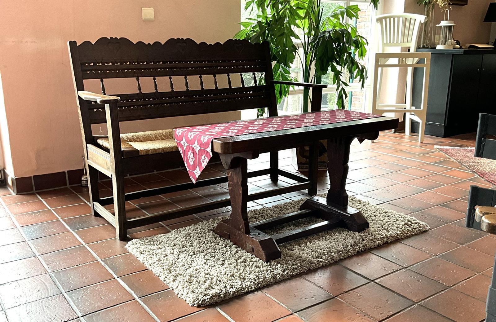 Holzbank und Tisch mit Tischdecke auf Teppich im Raum mit Terrakottaboden.