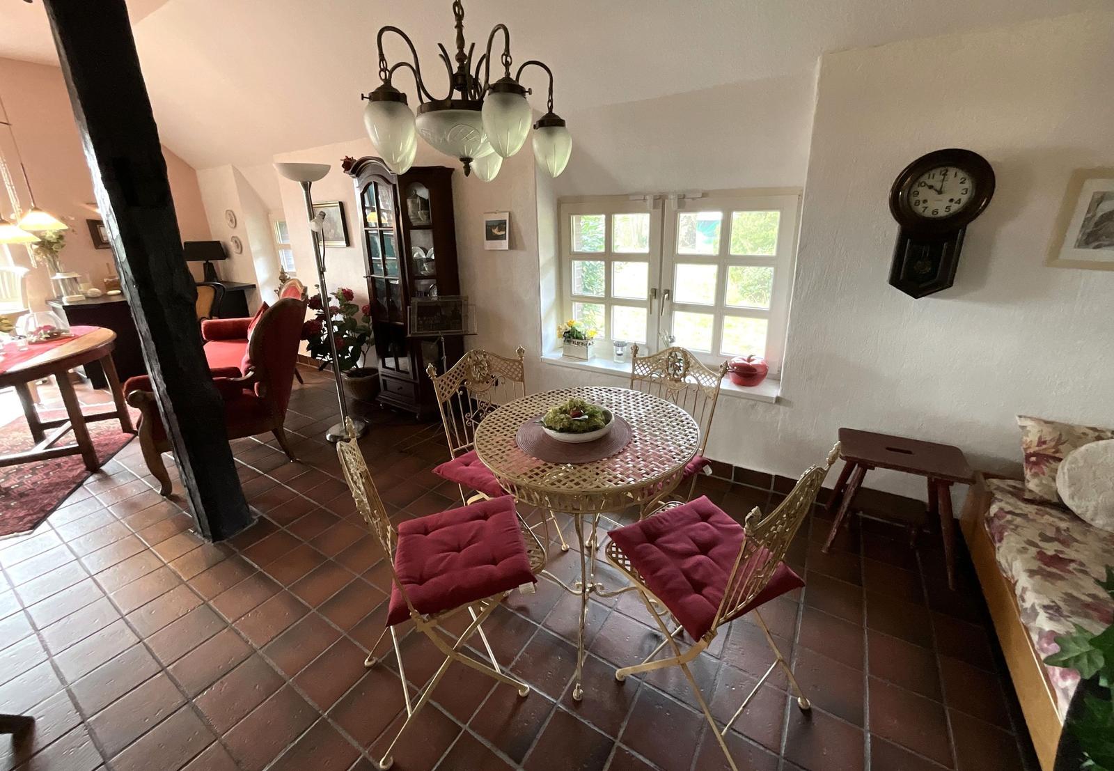 Essbereich mit runden Tisch und Stühlen, Fenster und Wanduhr.