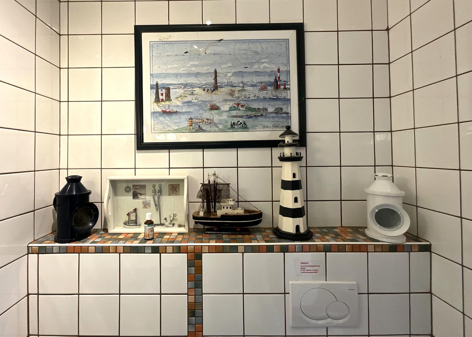 Bad mit Fliesenwand, Seemotivbild und Seehandwerk dekoriert.