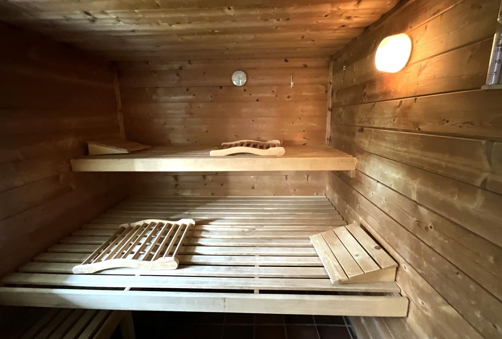 Sauna mit Holzbanken und Temperaturmessgerät an der Wand.