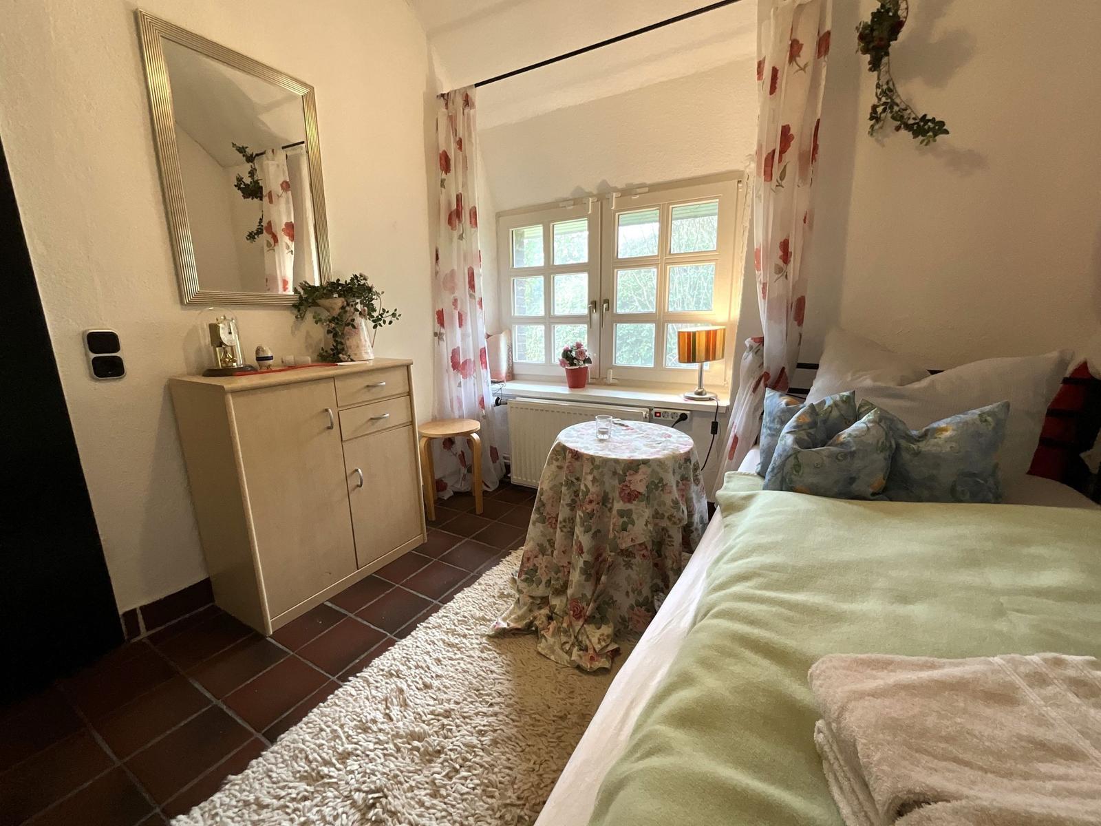 Schlafzimmer mit Bett, Schrank, Spiegel und Fenster mit Vorhängen.