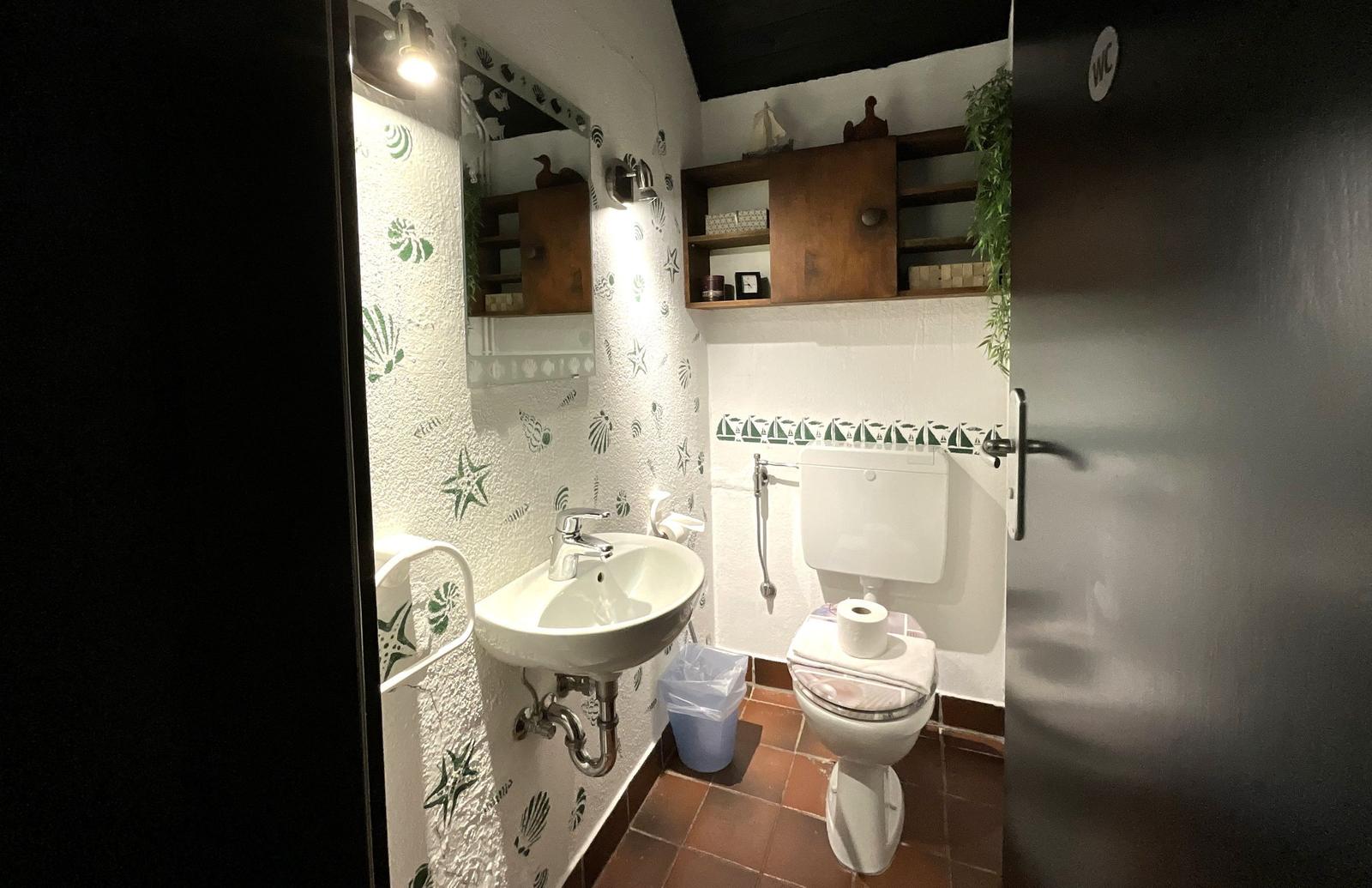 Badezimmer mit Waschbecken, Toilette und Holzregal an der Wand.