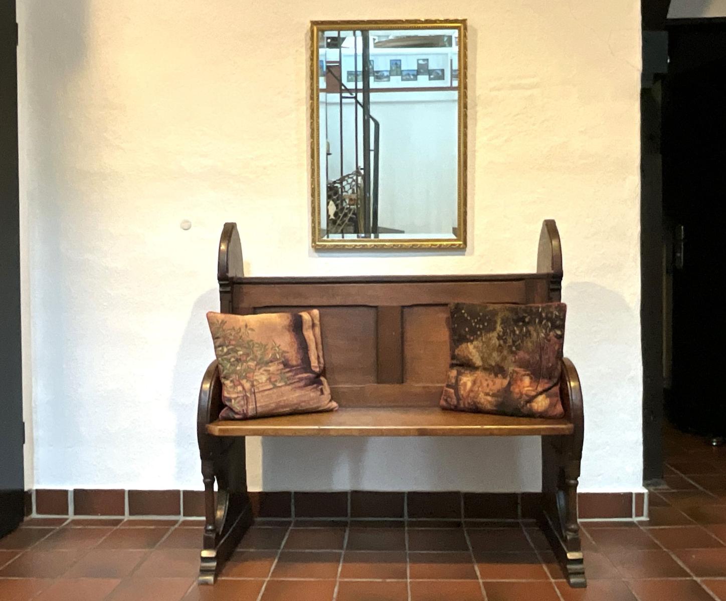 Holzbank mit zwei Kissen unter einem Spiegel an einer Wand.