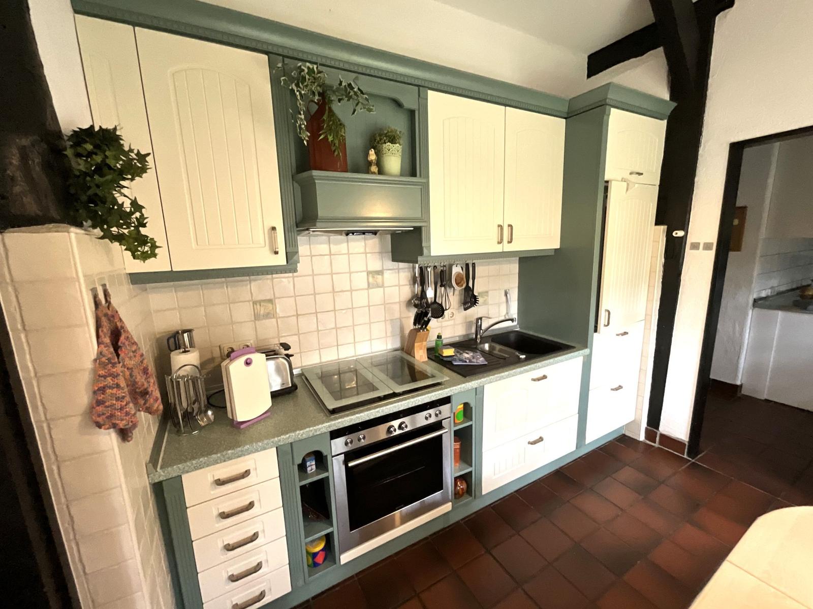 Küche mit weißen Schränken, grüner Arbeitsplatte und integriertem Ofen.