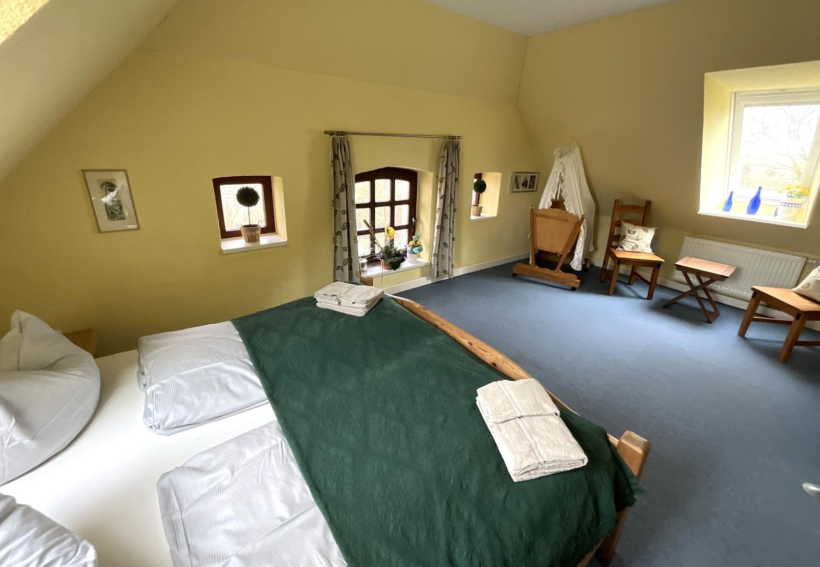 Schlafzimmer mit Bett, Fenstern und Holzmöbeln.