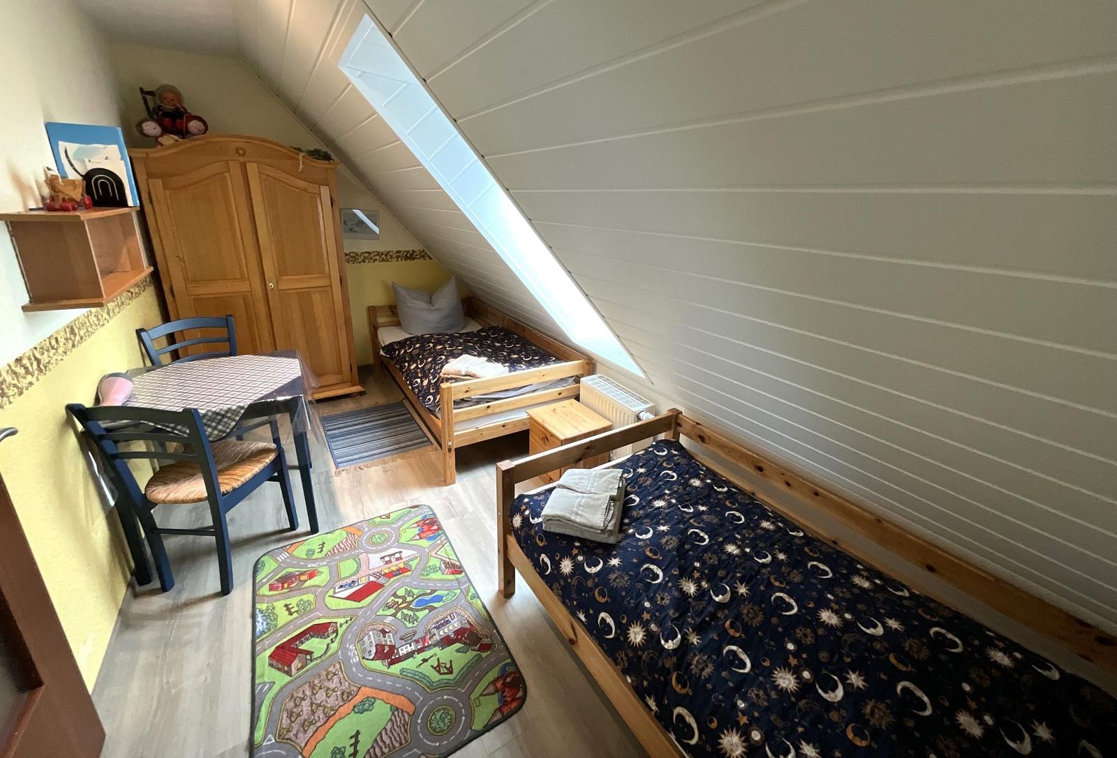 Zimmer mit zwei Betten, Tisch und Kleiderschrank unter Dachschrägen.