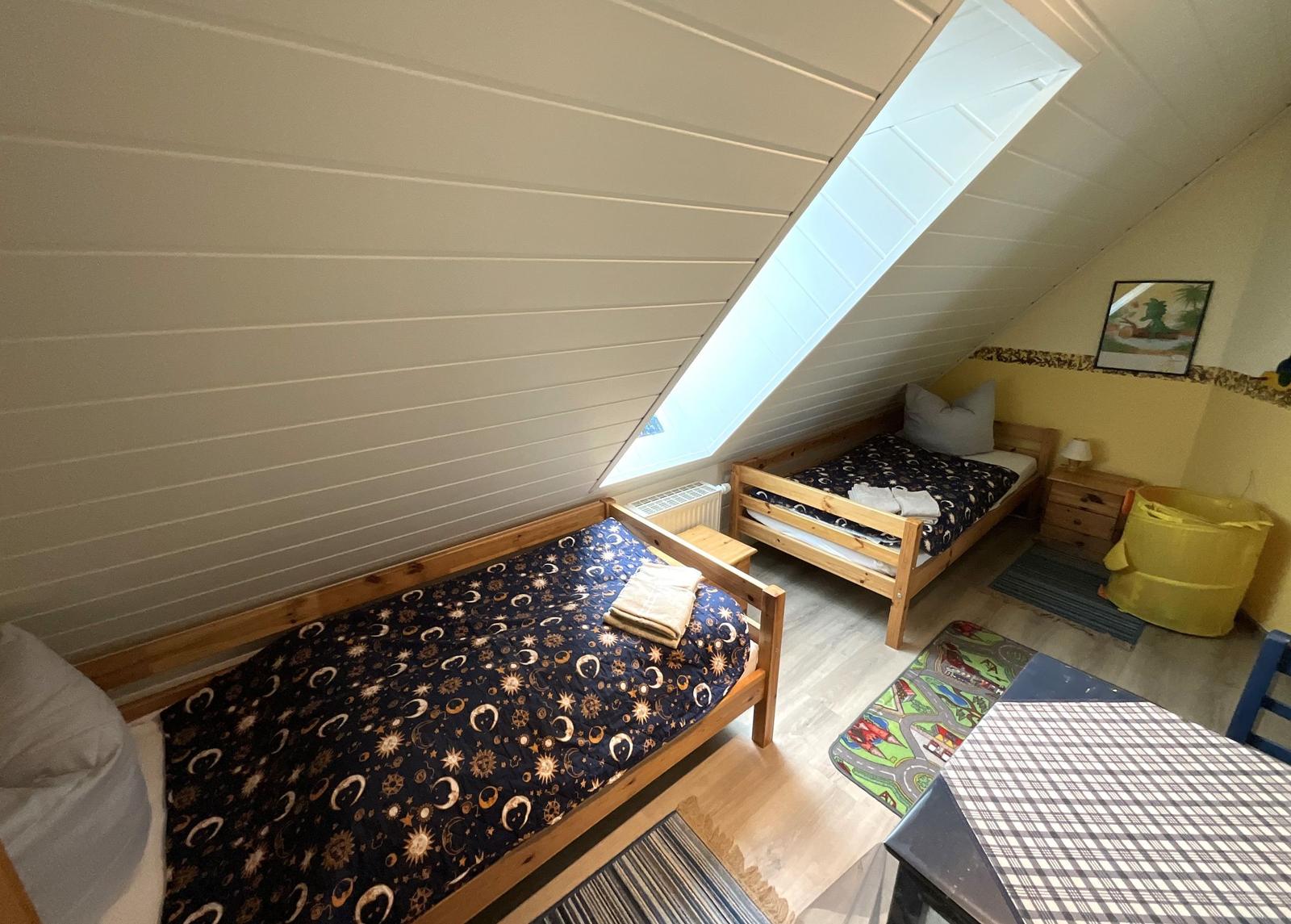 Zimmer mit zwei Betten, Dachschräge und Dachfenster. Holzbett, Teppich und Tisch.