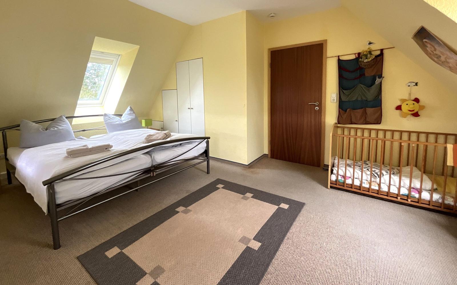 Schlafzimmer mit Dachschrägen, Bett, Kinderbett und Fenster