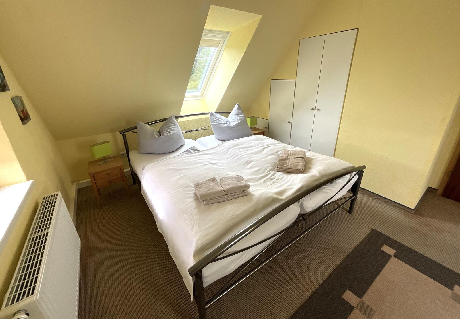 Doppelbettzimmer mit Dachschräge, Fenster, Kleiderschrank und Heizung.