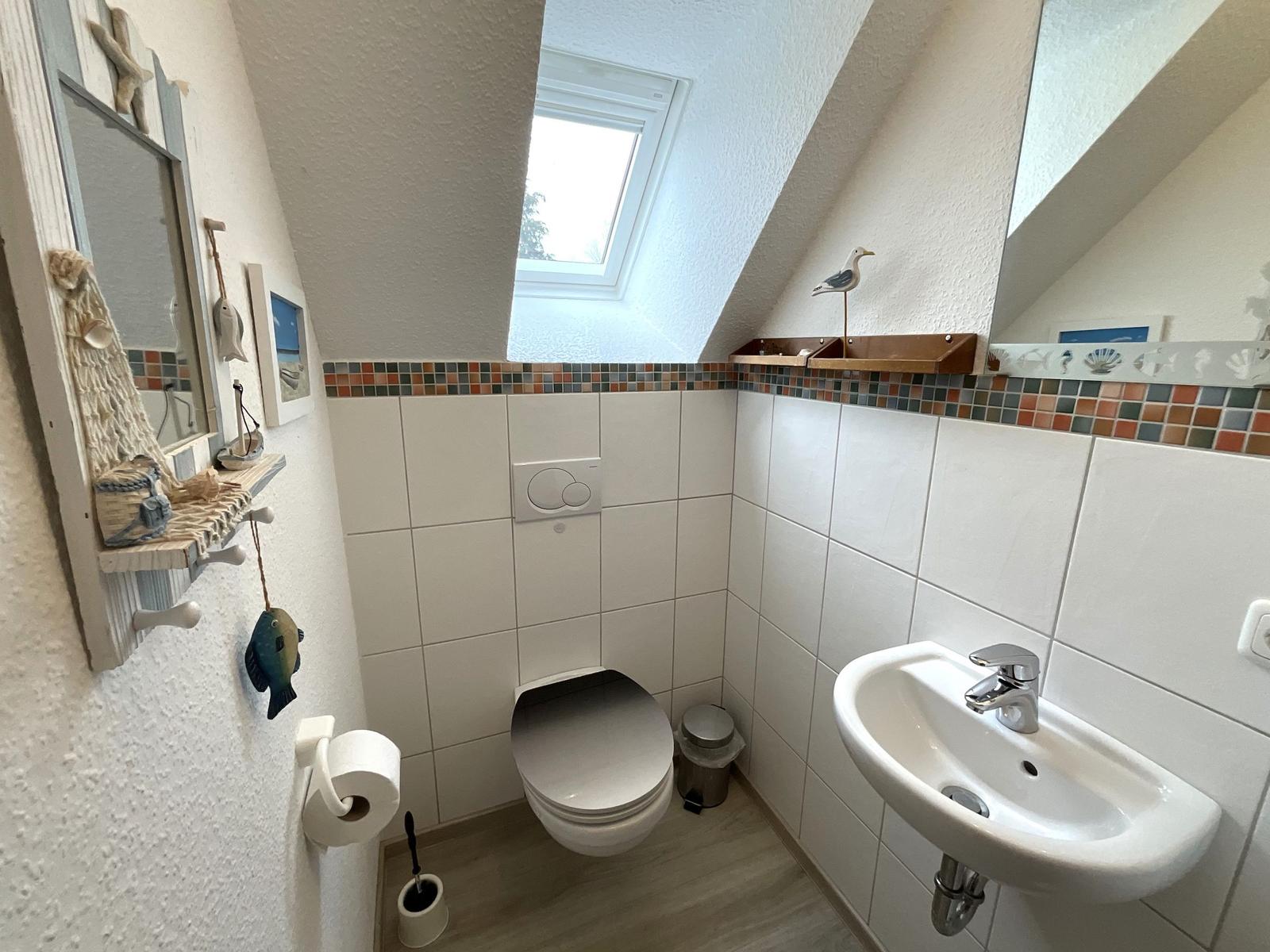 Badezimmer mit Toilette, Waschbecken und Dachfenster. Wandverkleidung mit Mosaikstreifen.