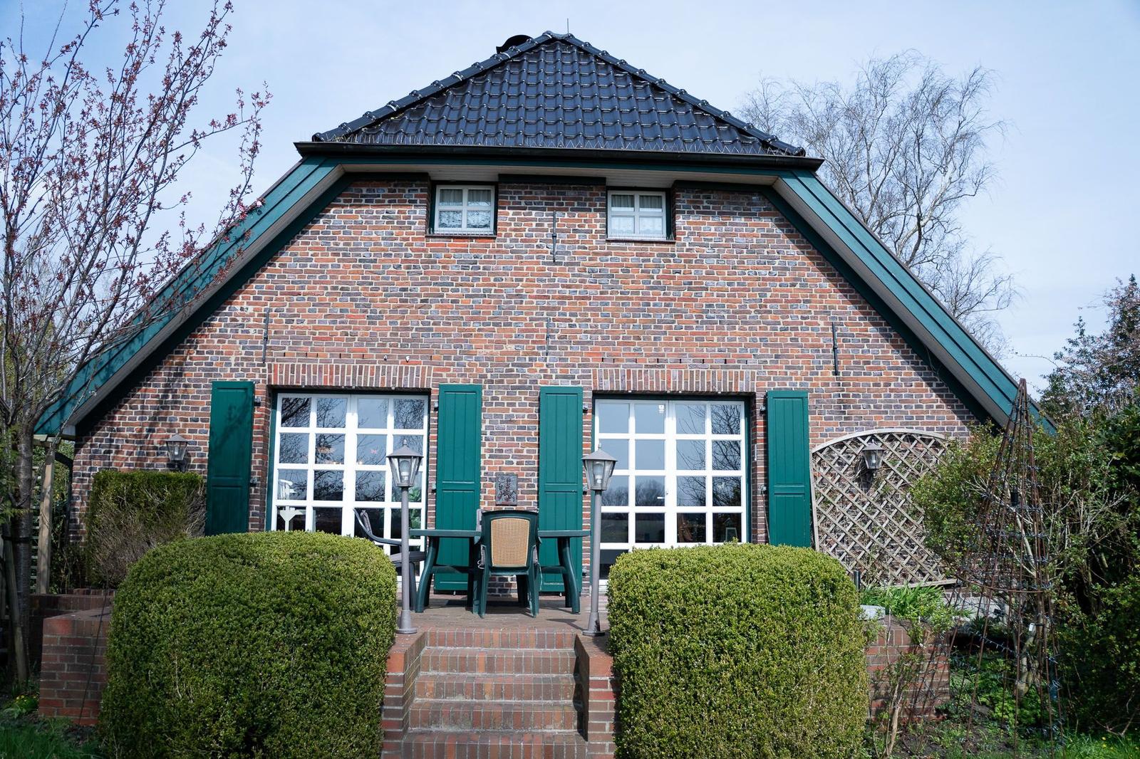Ein Haus mit Backsteinfassade und grünen Fensterläden. Vor dem Haus steht ein Tisch mit Stühlen.