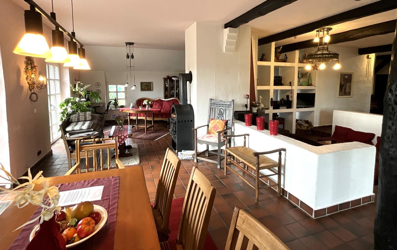 Wohn- und Essbereich mit Holztisch, Stühlen und Kaminofen. Terrakottaboden und Holzbalken.