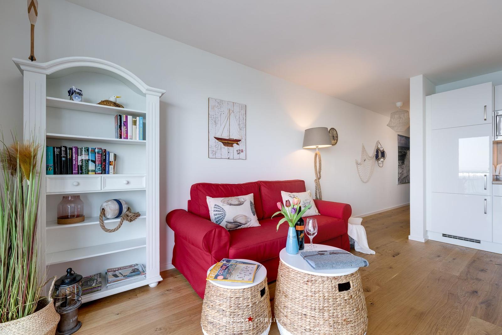 Ein Wohnzimmer mit rotem Sofa, weißen Regalen und Holzboden.