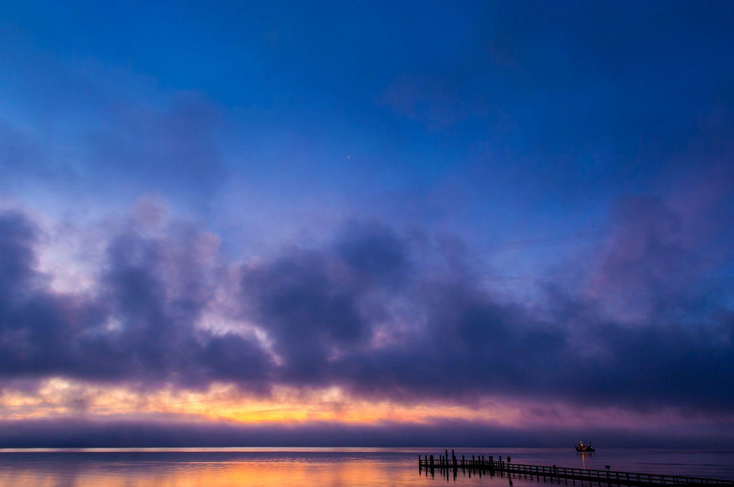Sonnenuntergang über ruhigem Wasser mit Dock und Boot.