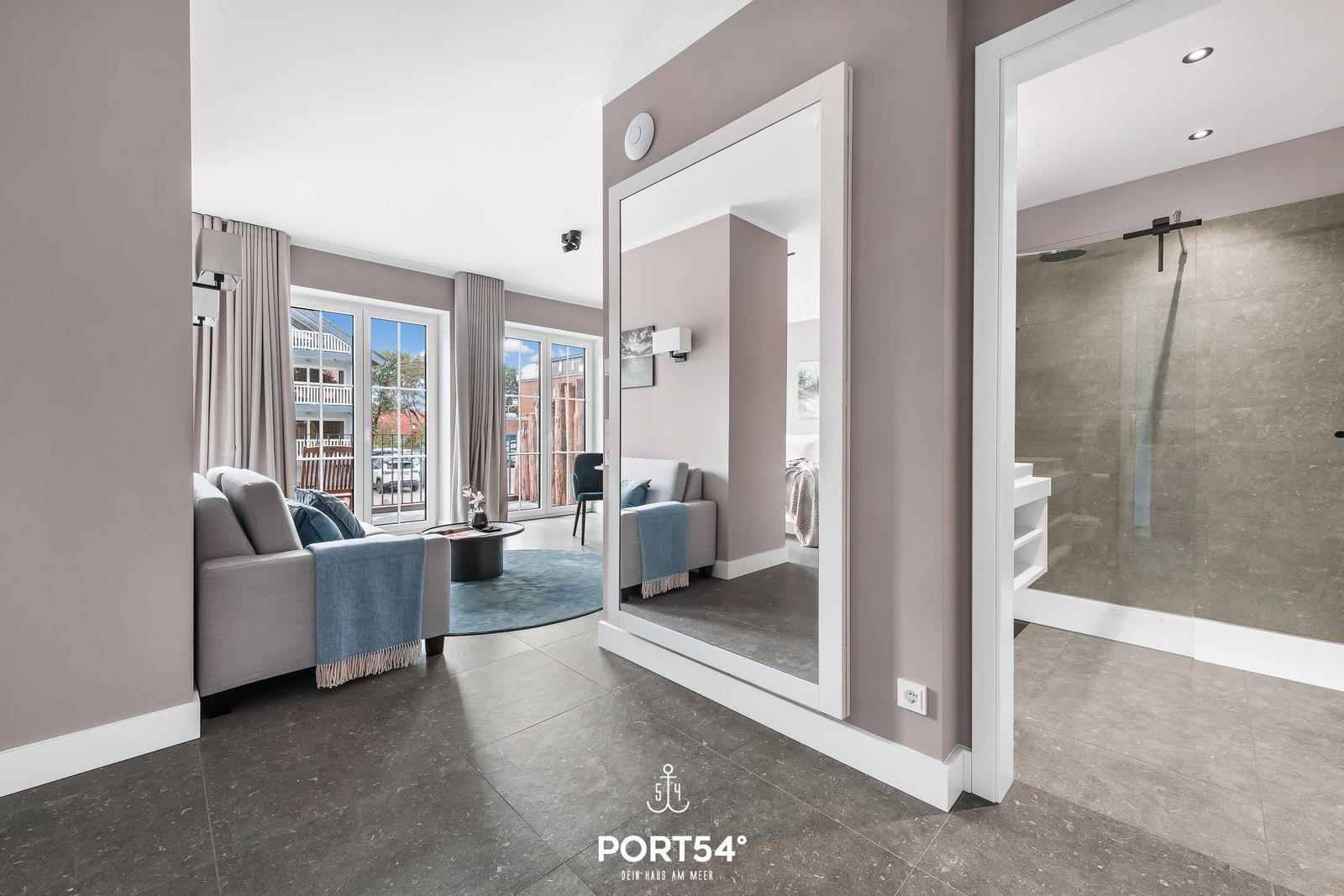 Wohnbereich mit Sofa, Spiegel und Dusche im Hintergrund.