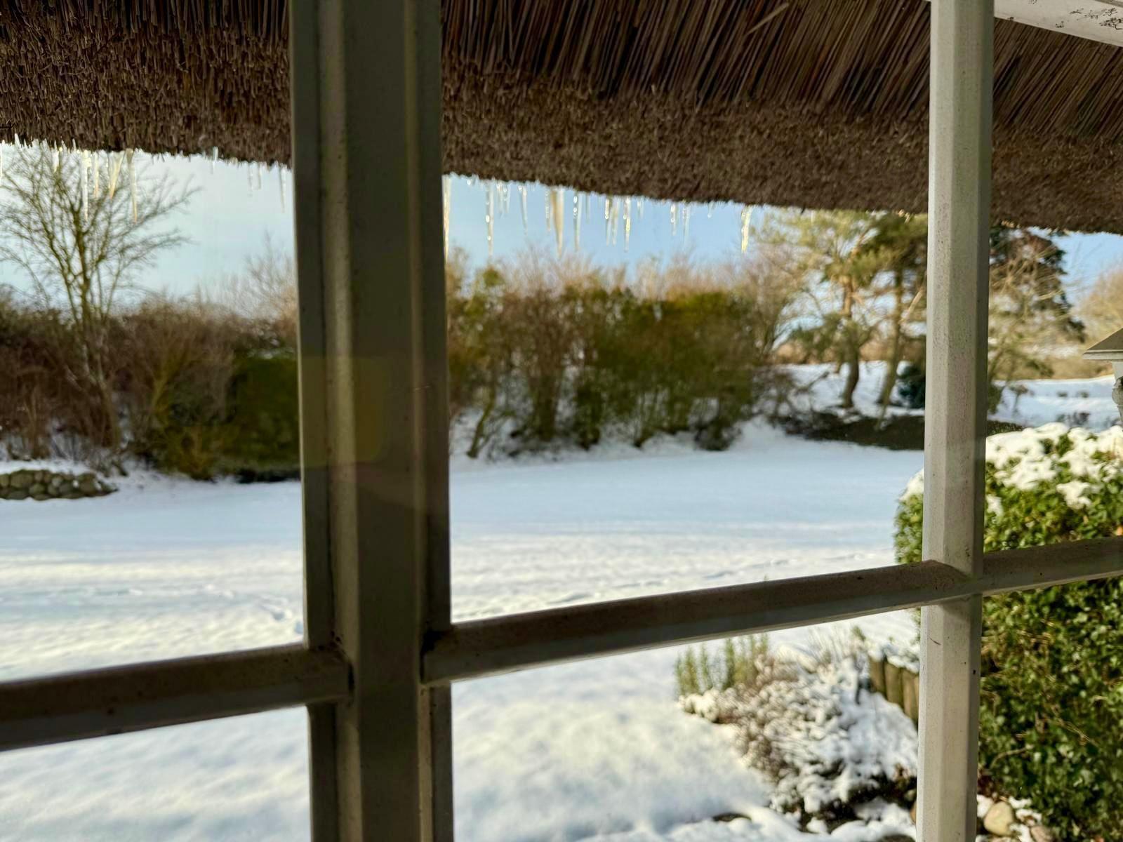 Schneebedeckter Garten mit Eiszapfen unter einem Strohdach