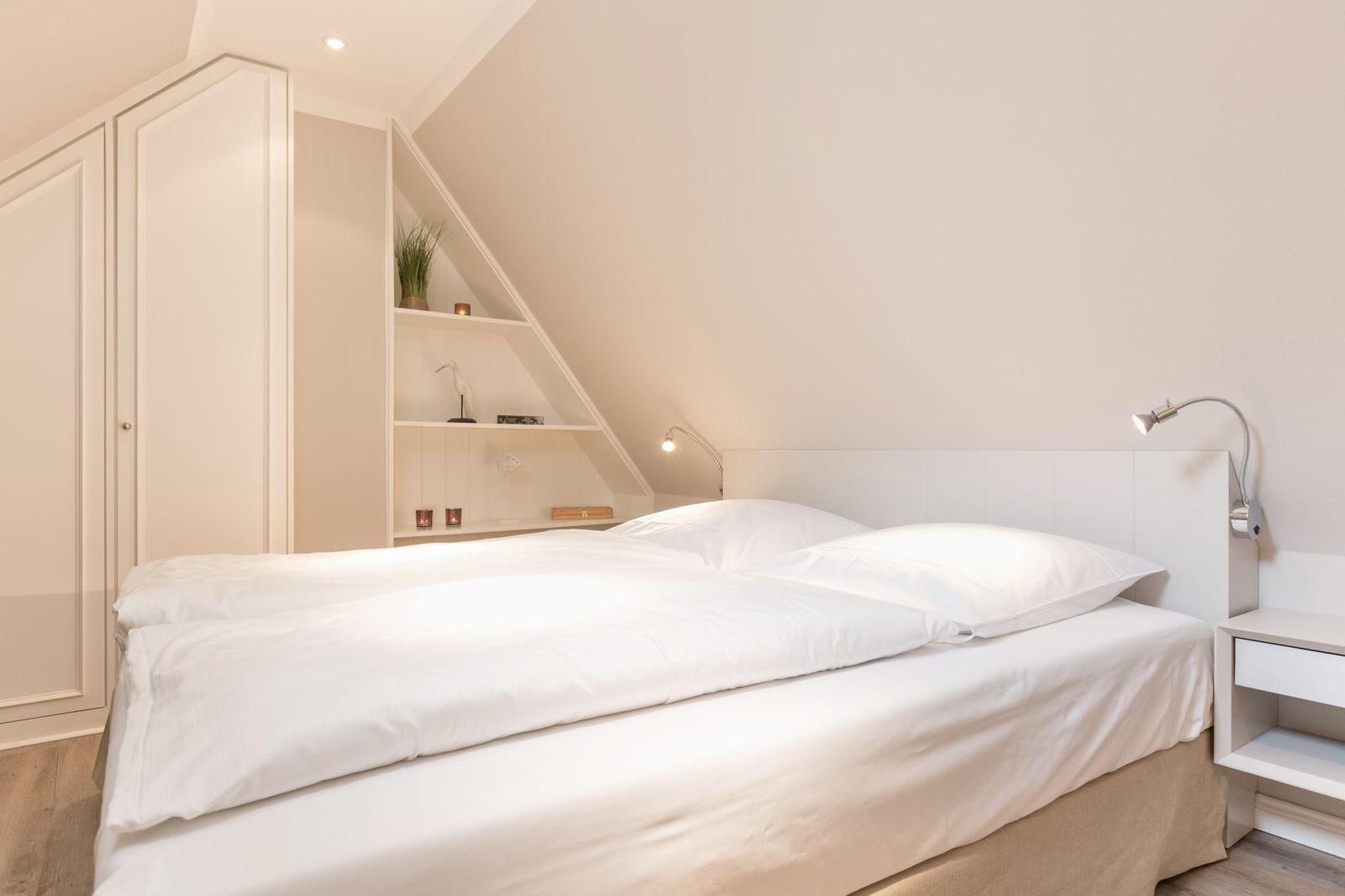 Schlafzimmer mit Doppelbett, Kleiderschrank und Regal unter Dachschräge.