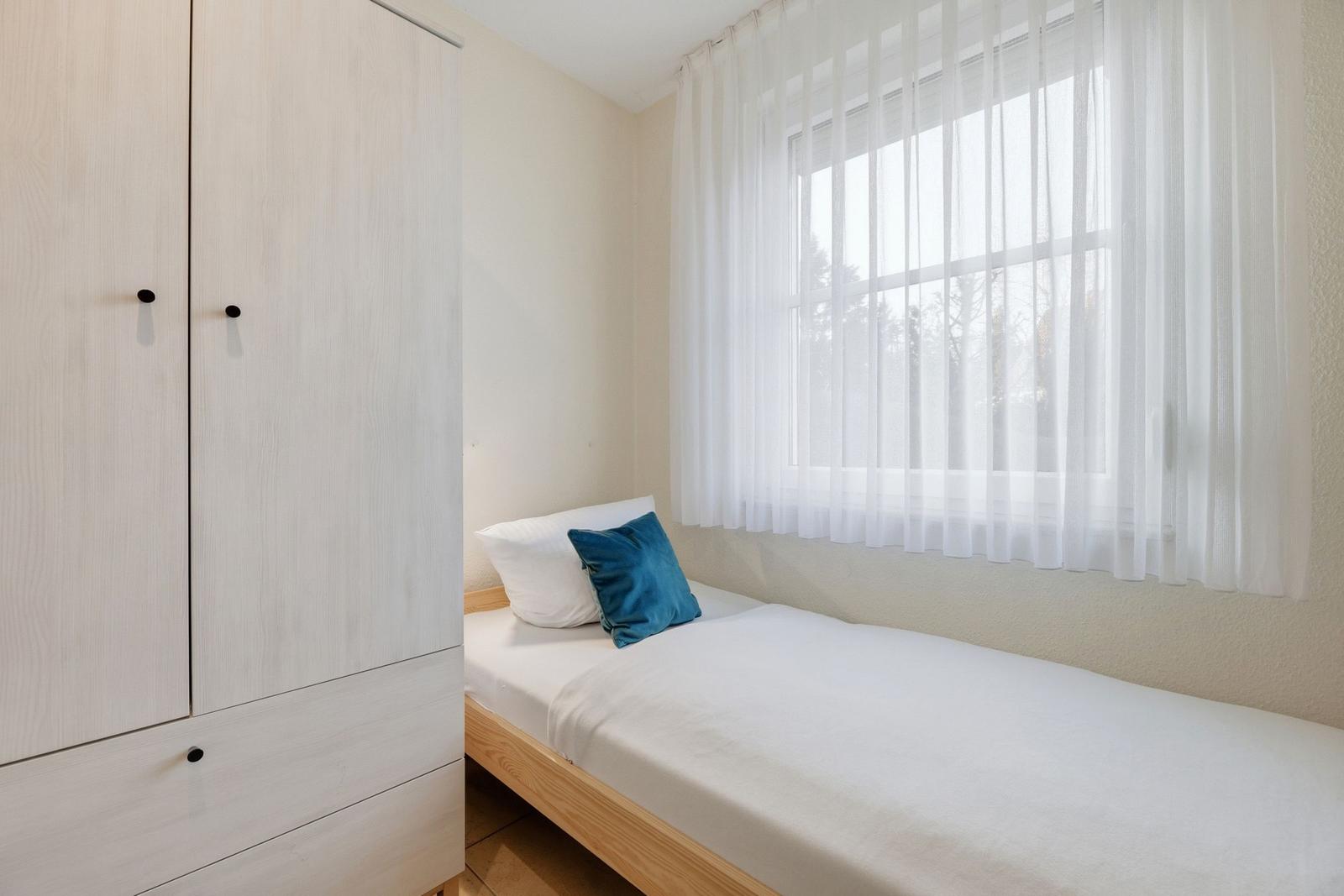 Schlafzimmer mit Bett, Kleiderschrank und Fenster mit Vorhängen.