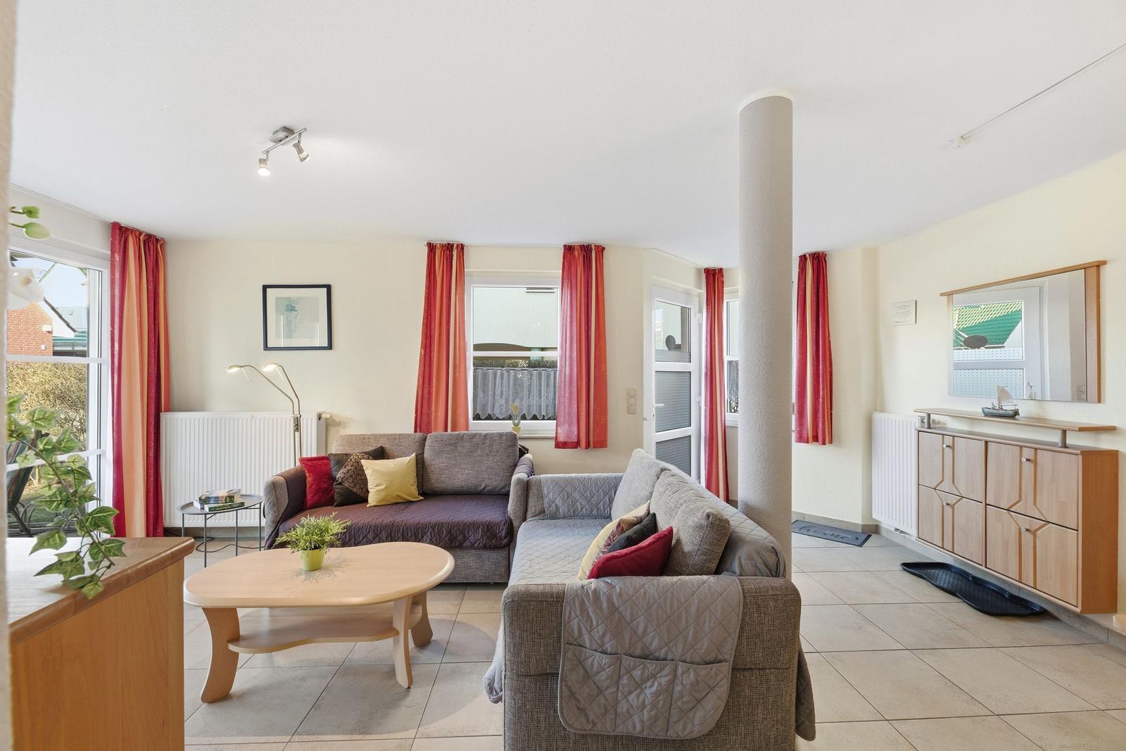 Wohnzimmer mit Sofa, Couchtisch und Fenstern mit roten Vorhängen.