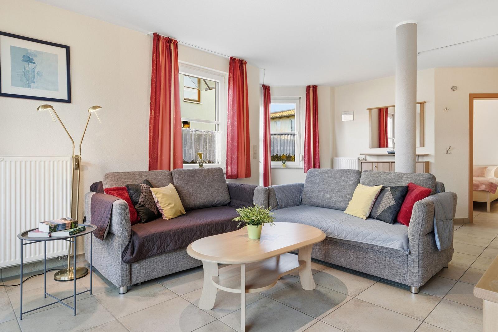 Wohnzimmer mit grauem Sofa, roten Vorhängen und Holztisch.
