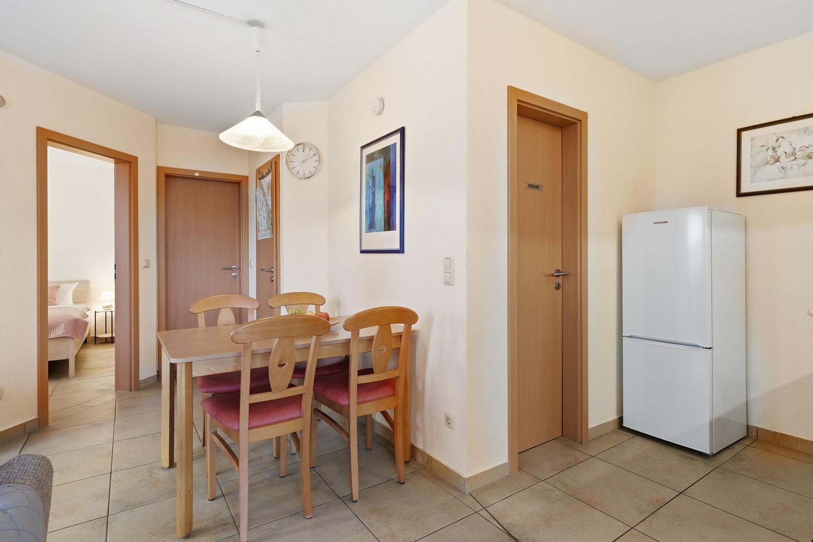 Essbereich mit Tisch, Stühlen und Kühlschrank. Tür führt in Schlafzimmer.