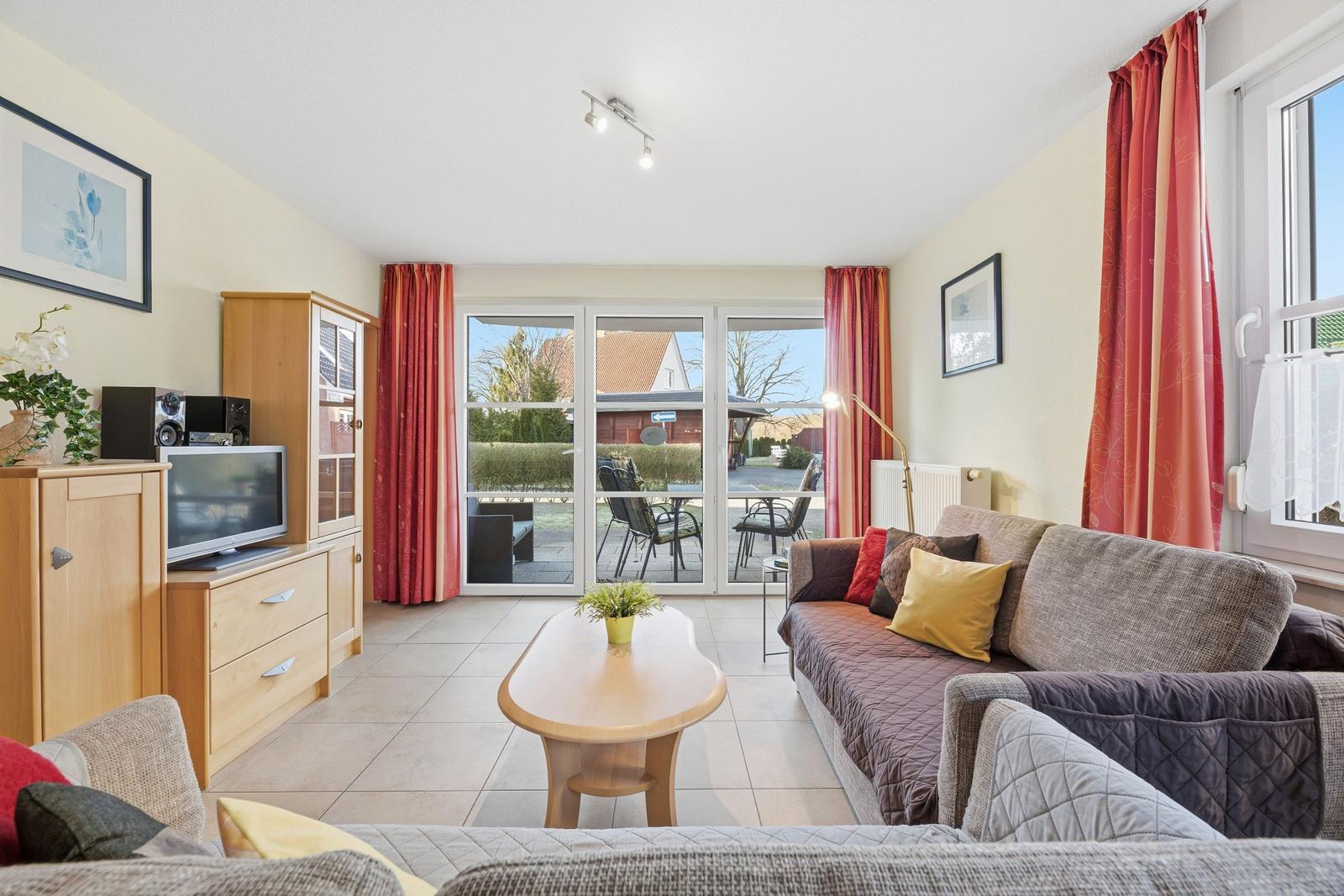 Wohnzimmer mit Sofa, Couchtisch und TV. Terrasse mit Gartenblick.