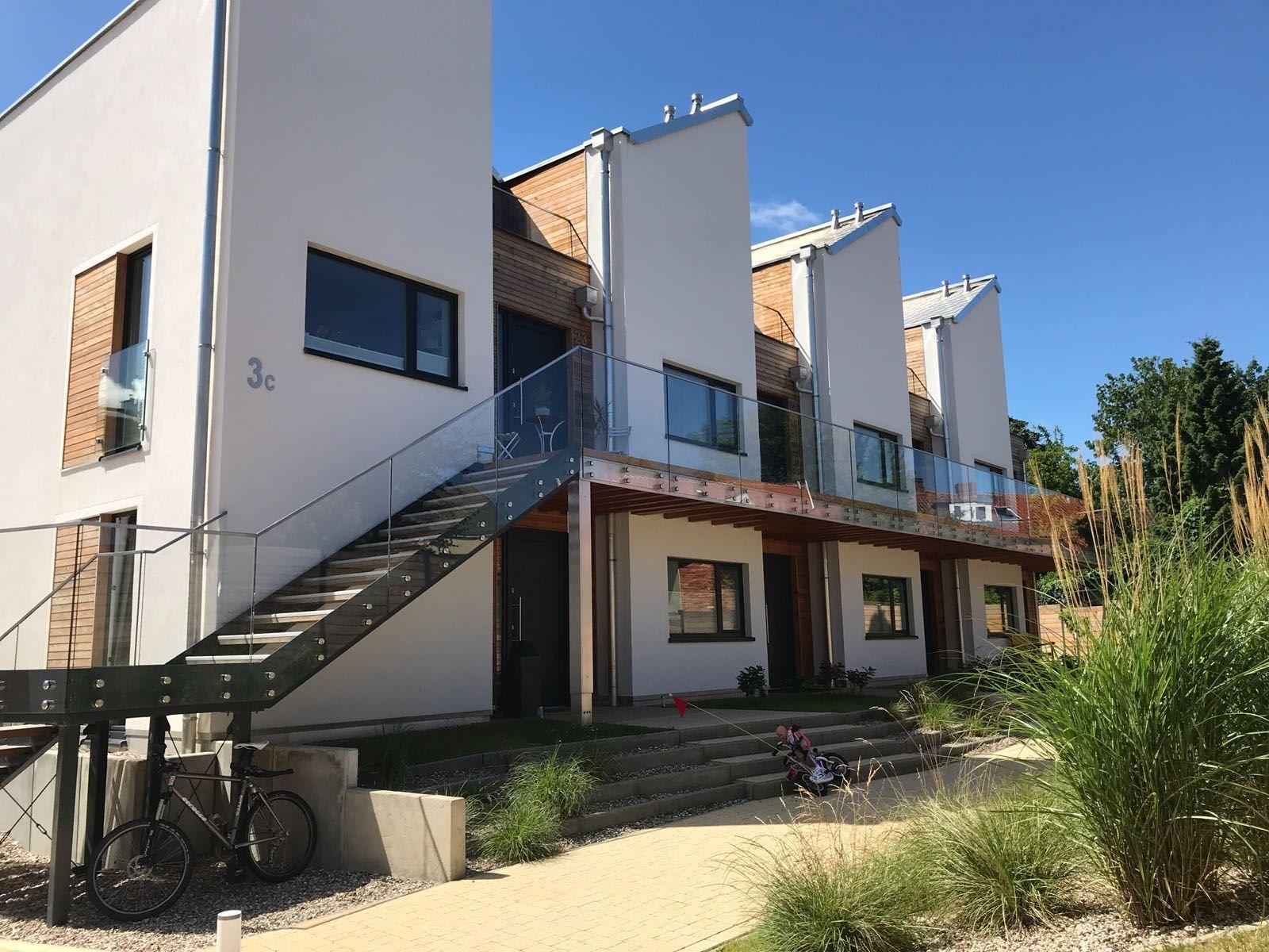 Moderne Wohnung mit Glasbrüstung und Holzverkleidung. Außentreppe und begrünte Fläche.