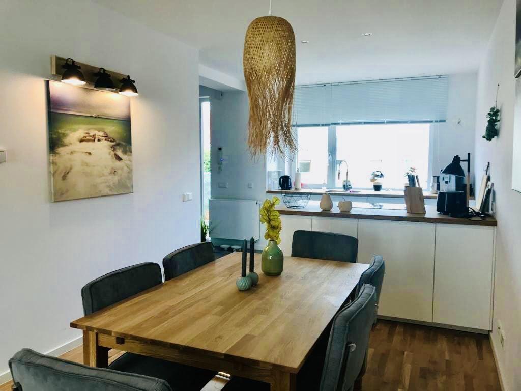 Essbereich mit Holztisch, Stühlen und Küchenzeile im Hintergrund.