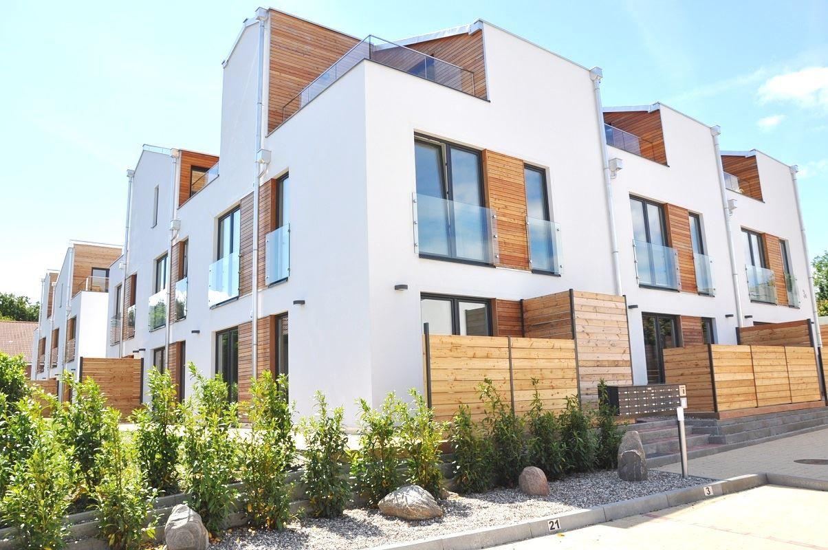 Moderne Wohnhäuser mit Holzverkleidung und Balkonen. Grünflächen und Steine im Vorgarten.